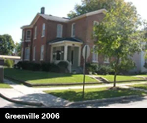 A large brick house with a front porch, surrounded by green grass and trees, under a clear blue sky depicting Good Samaritan Home's housing expansion for those looking for re-entry. 