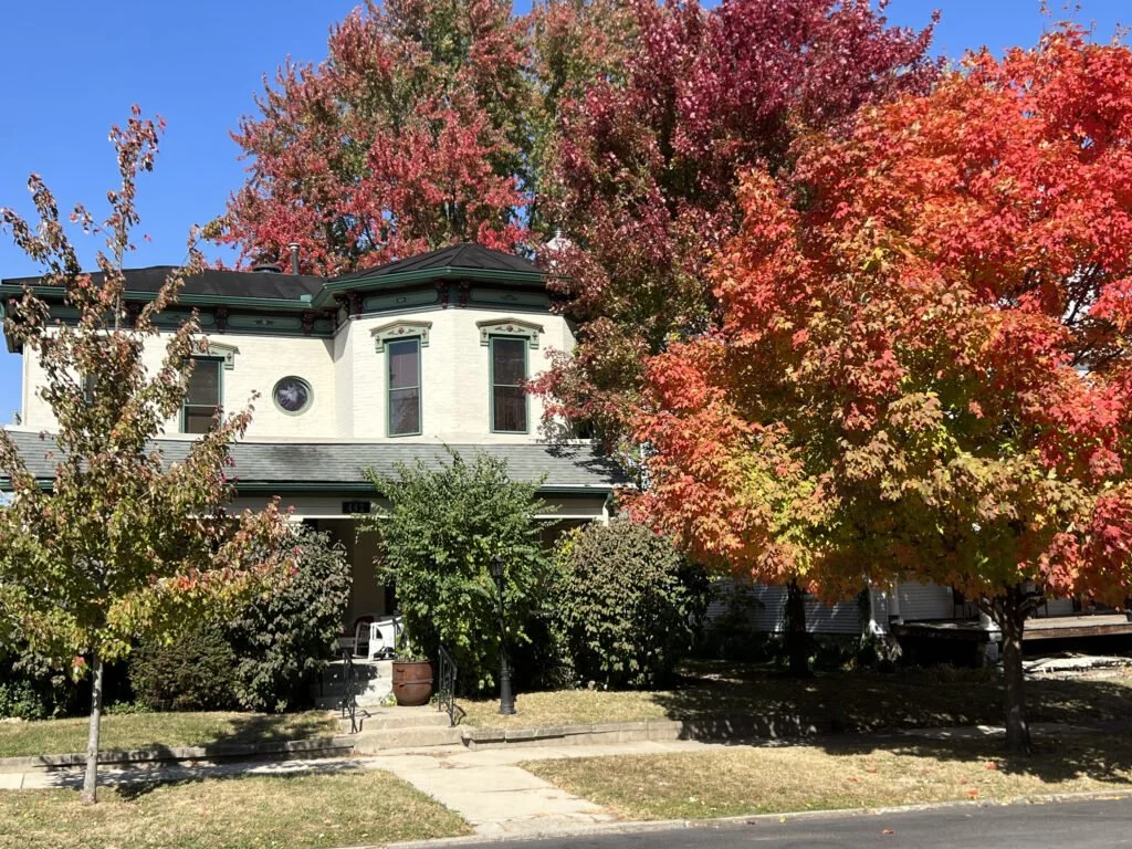 A house with white walls and dark green trim, surrounded by trees with colorful autumn leaves, on a sunny day depicting Good Samaritan Home's housing expansion for those looking for re-entry. 
