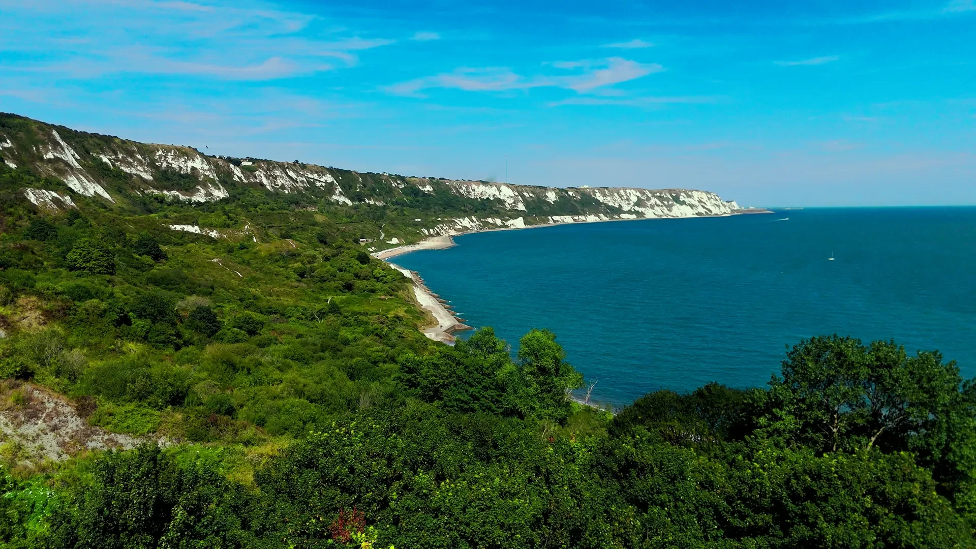 White chalk cliffs along a green hillside overlooking the blue ocean under a partly cloudy sky.