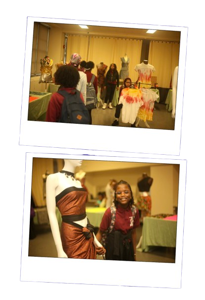 People browsing and shopping at a craft or fashion fair with display tables and mannequin dressed in colorful clothing.