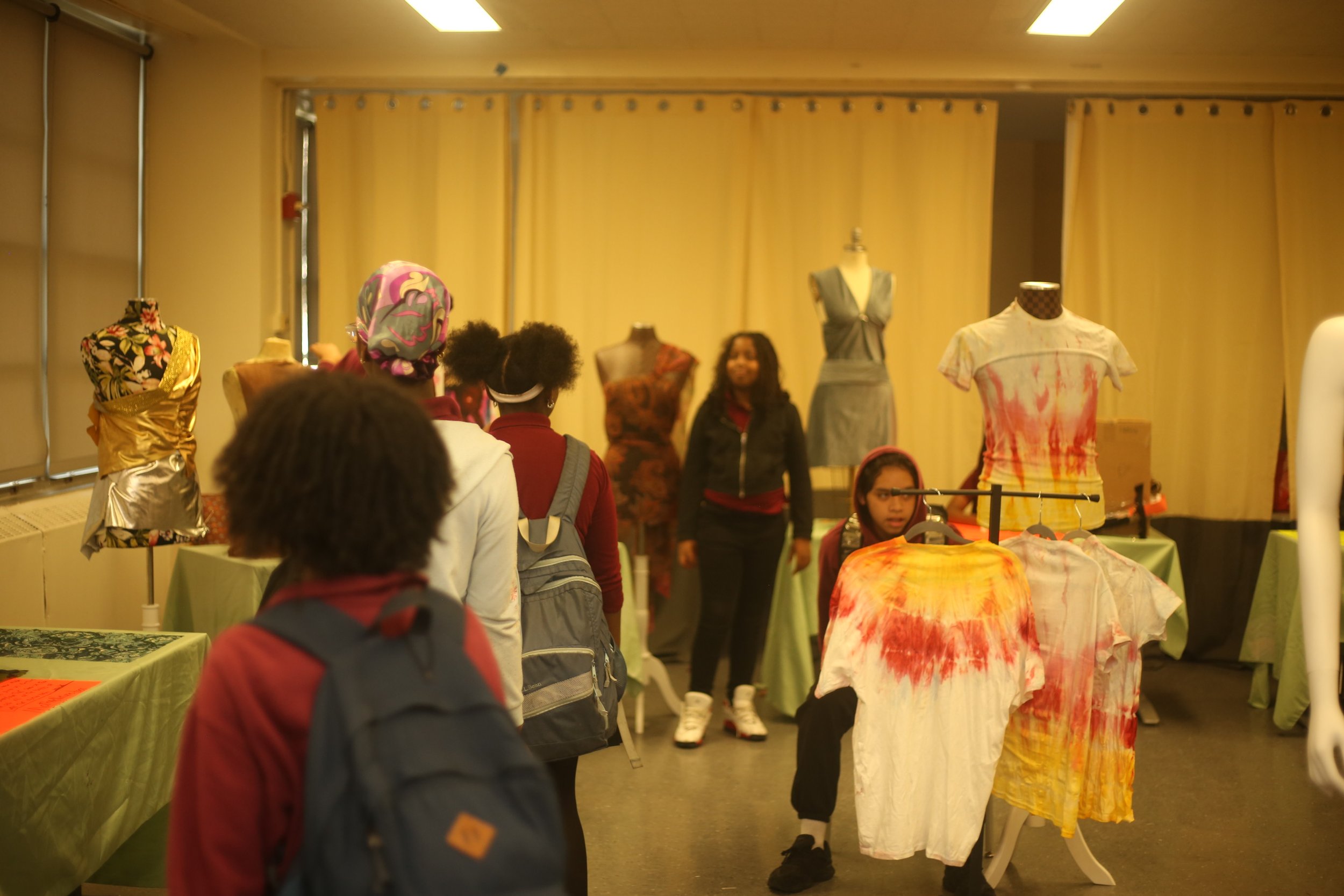 People attending a fashion showcase or display, viewing mannequins wearing colorful and patterned clothing in an indoor venue.