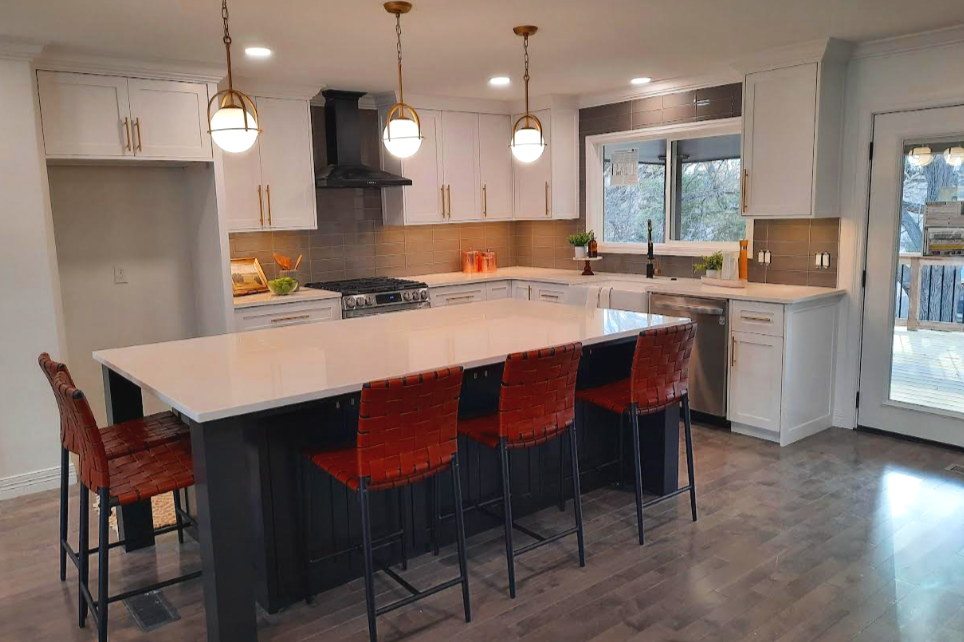 Modern kitchen with white cabinets, a white island with black base, four red woven bar stools, pendant lights above the island, a stove with a range hood, a window, and a sliding glass door leading outside.