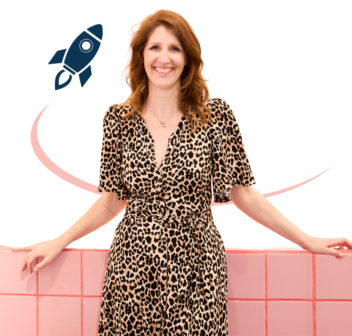 Eine lachende Frau in einem leopardmuster Kleid steht vor einer pinken Wand und lehnt an einer Mauer.