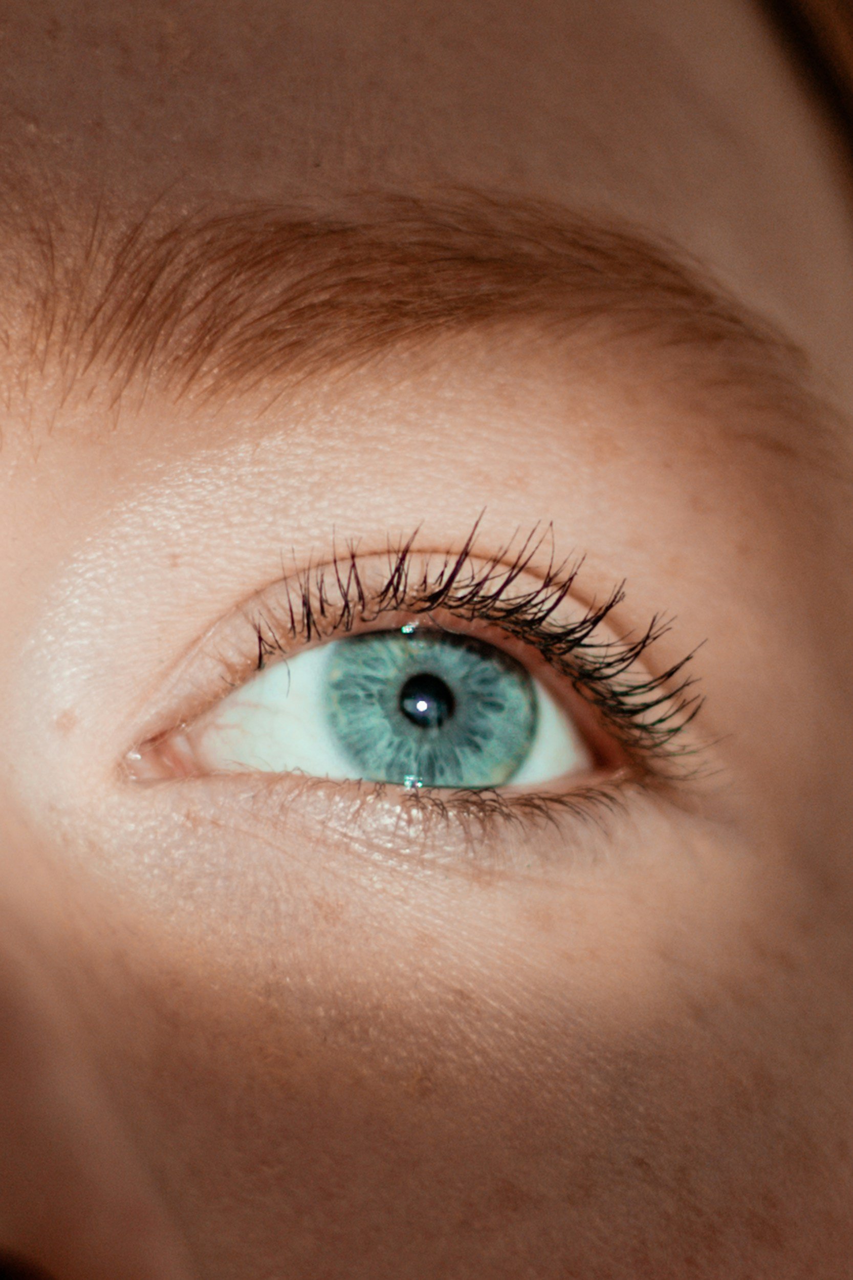 Close-up of a person's blue eye with long eyelashes and light skin.