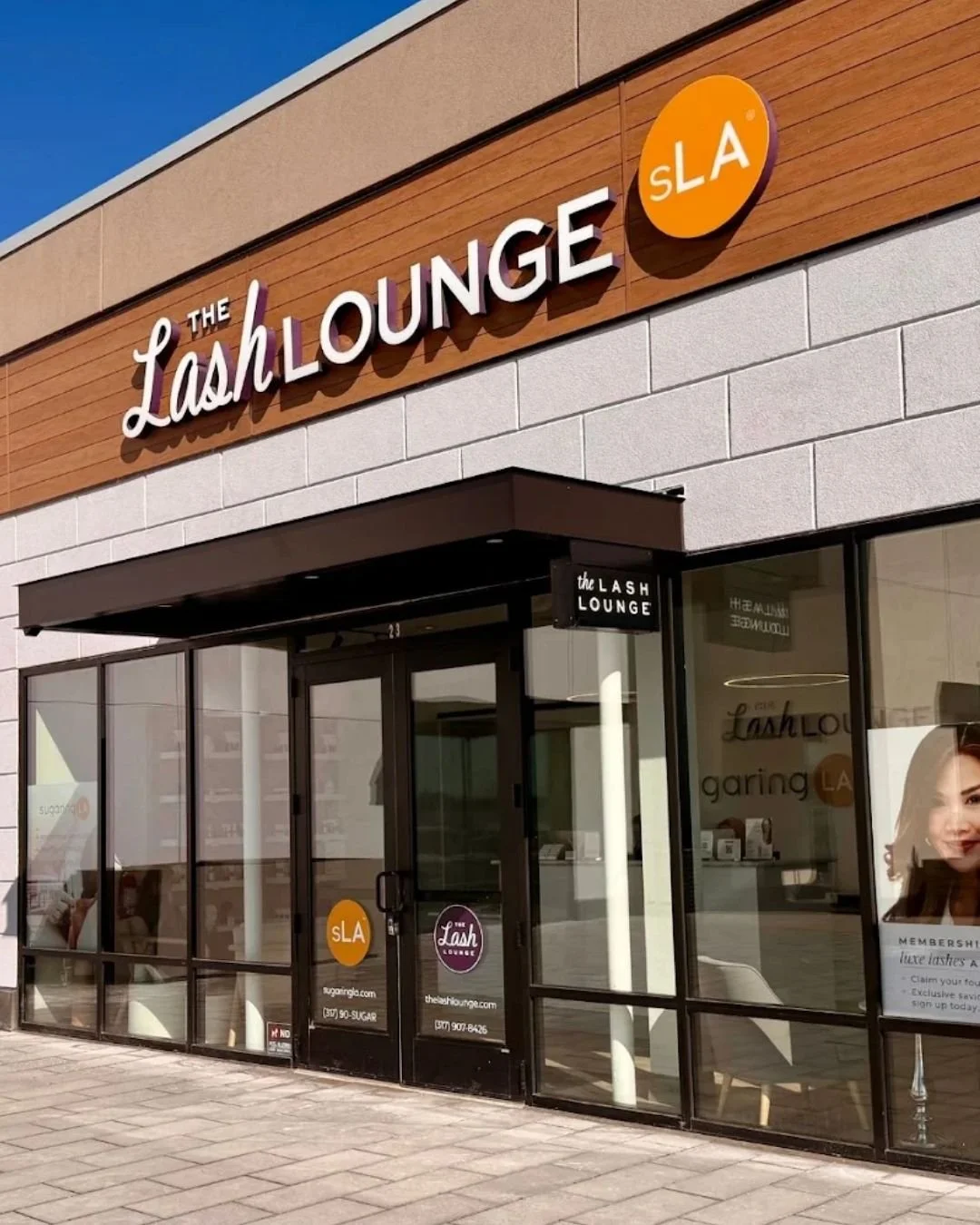 Exterior view of The Lash Lounge salon storefront with signage and glass doors, located in a strip mall on a sunny day.