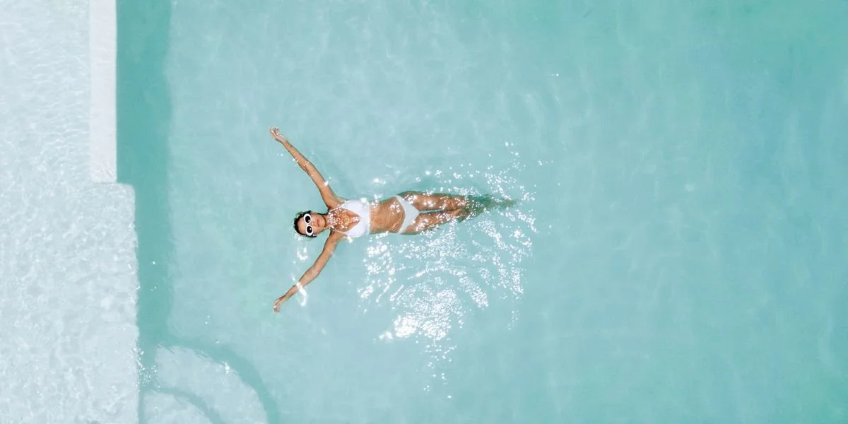 A woman in a white swimsuit with goggles swimming in a pool.