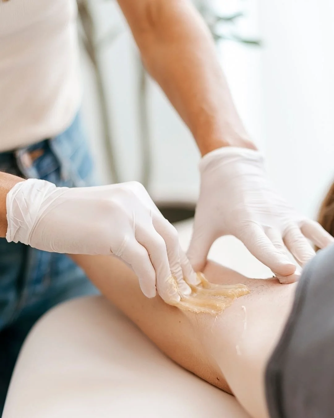 A person receiving a waxing treatment on their leg by an esthetician wearing gloves.