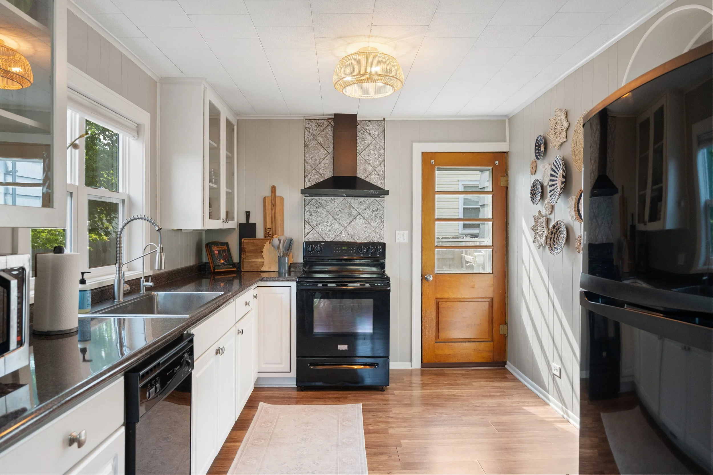 A kitchen with white cabinets, black stove, wooden door, and wall decorations.