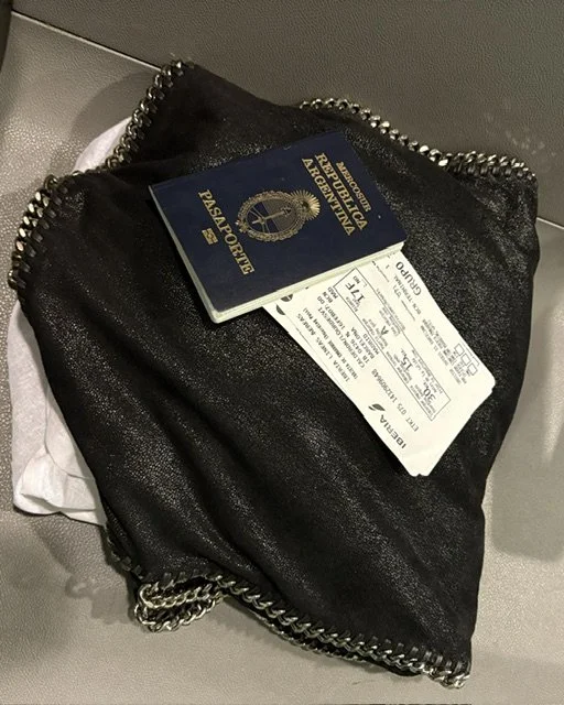 Una bolsa negra con una cremallera de cadena visible, con un pasaporte, un boleto de avión y una tarjeta de embarque encima.
