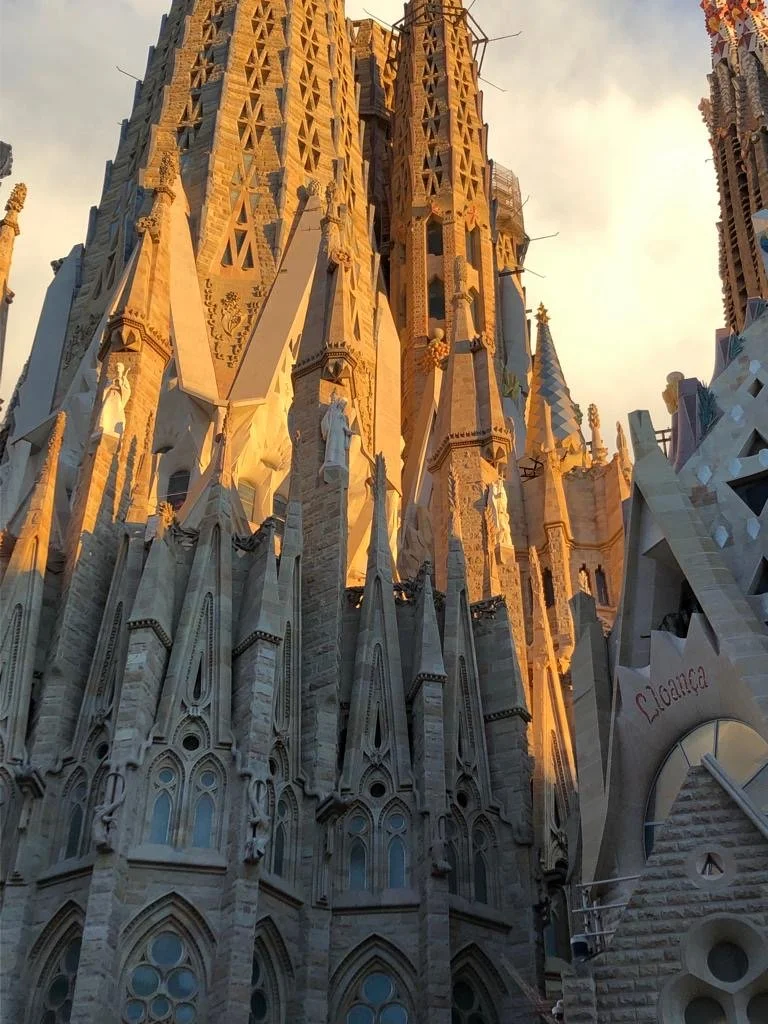 Vista de la fachada de la iglesia de La Sagrada Familia en Barcelona, con detalles arquitectónicos góticos y modernistas, durante el atardecer.