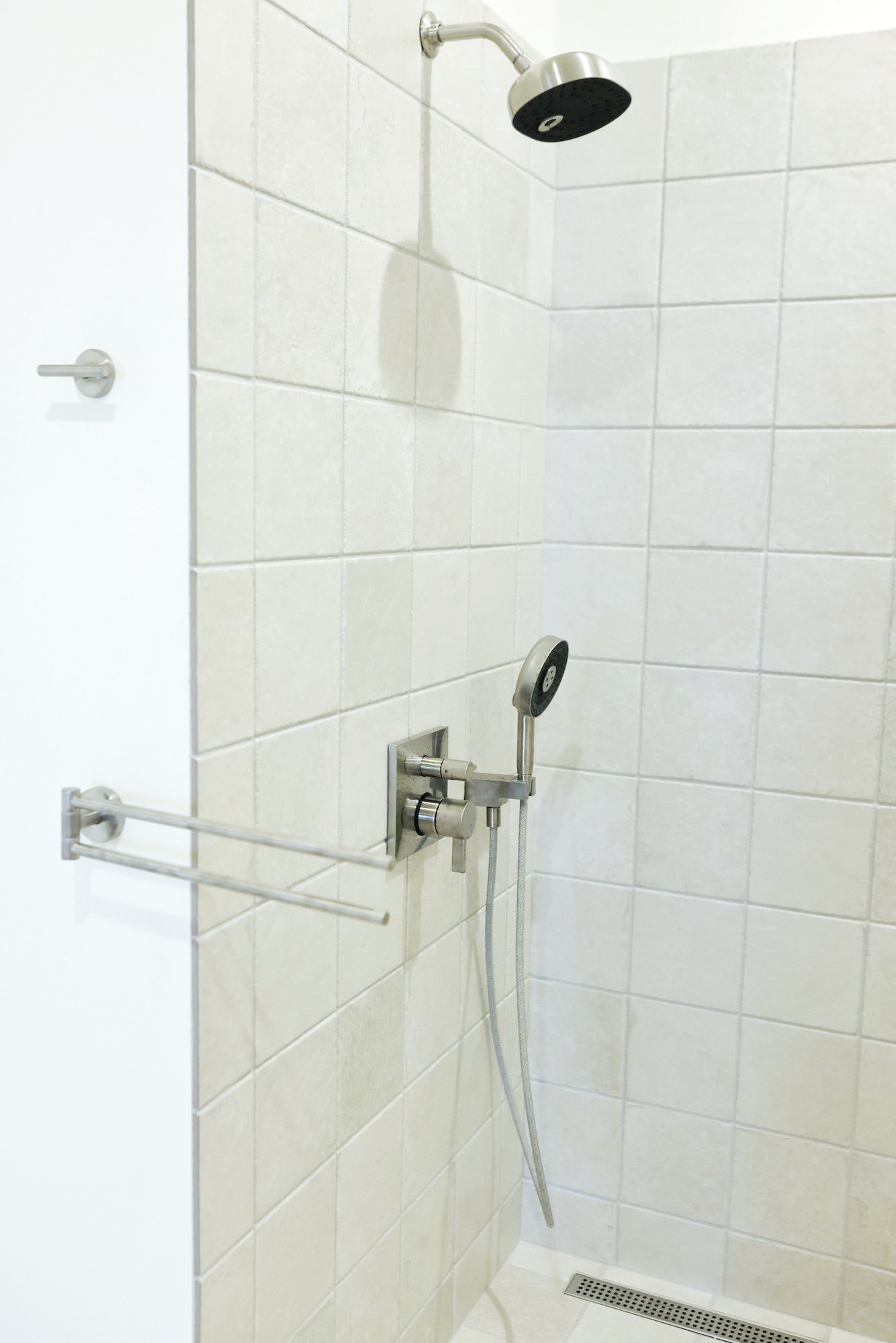 Shower with two showerheads, a hand-held shower, and grab bars in a tiled bathroom