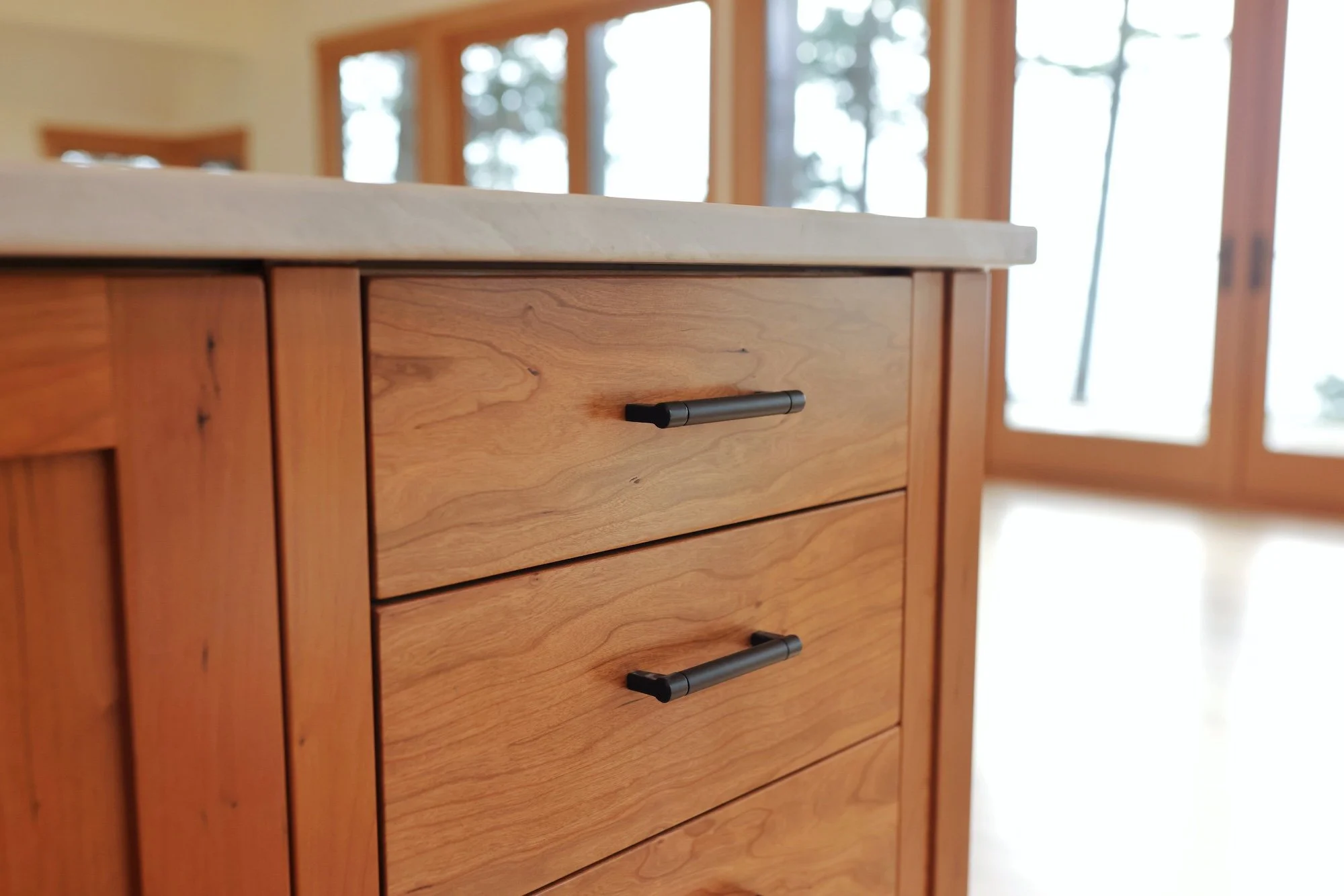 Close-up of a wooden dresser with black handles in a room with large windows and natural light.