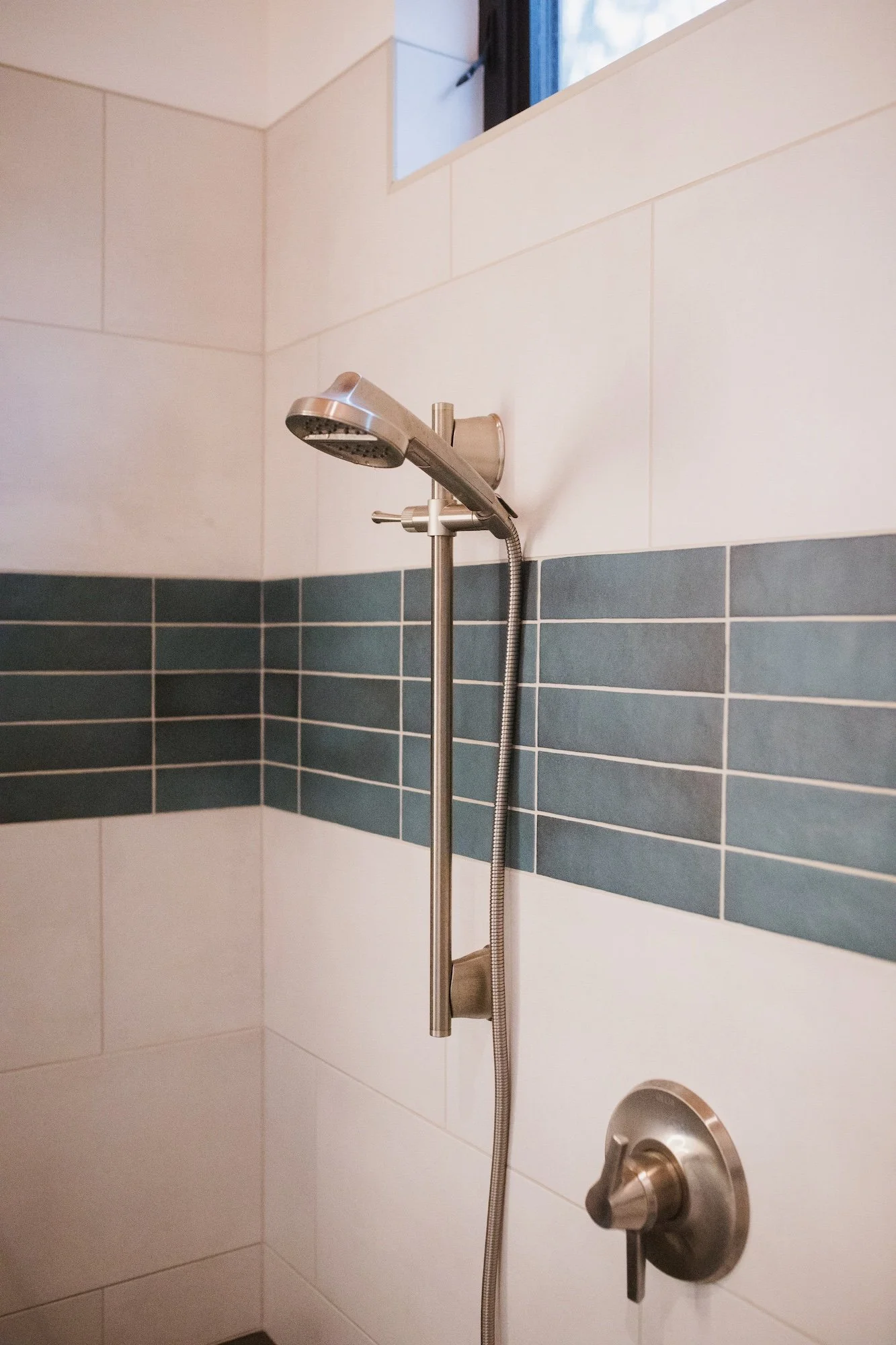 A shower with a handheld showerhead mounted on a wall, featuring a modern brushed metal finish, against beige and blue tiled walls.