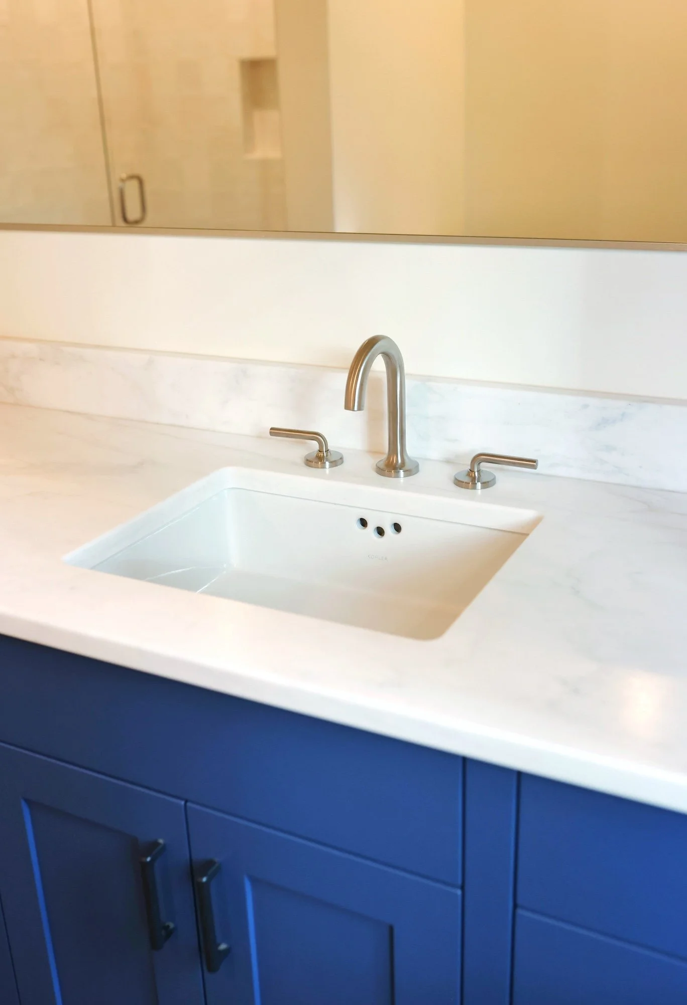 Close-up of a bathroom vanity with a white marble countertop, a white undermount sink, and a modern brushed nickel faucet; the cabinet below is painted dark blue.