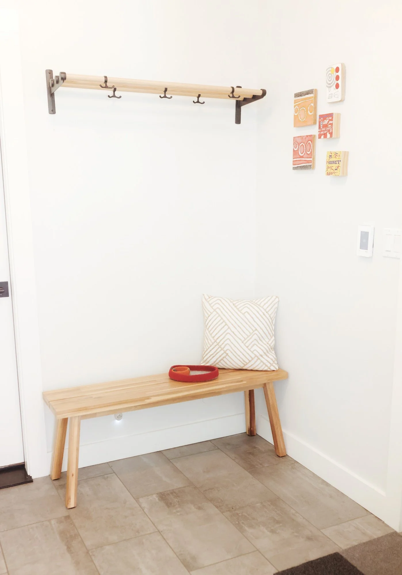 Entryway with a wooden bench, a pillow, a red leash, a wall-hanging with hooks, and decorative wall art.