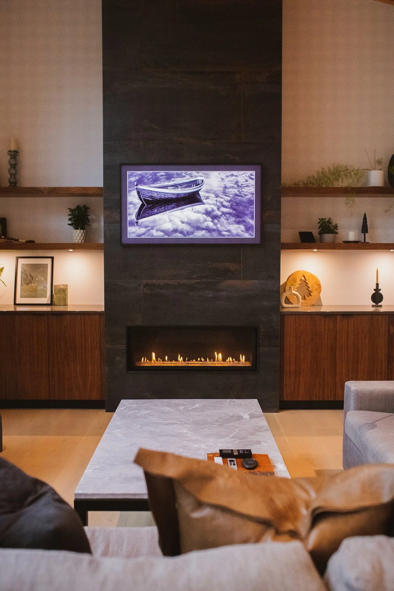 Living room with a mounted TV displaying a boat on water, a fireplace, framed pictures, decorative items, and a coffee table in the foreground.