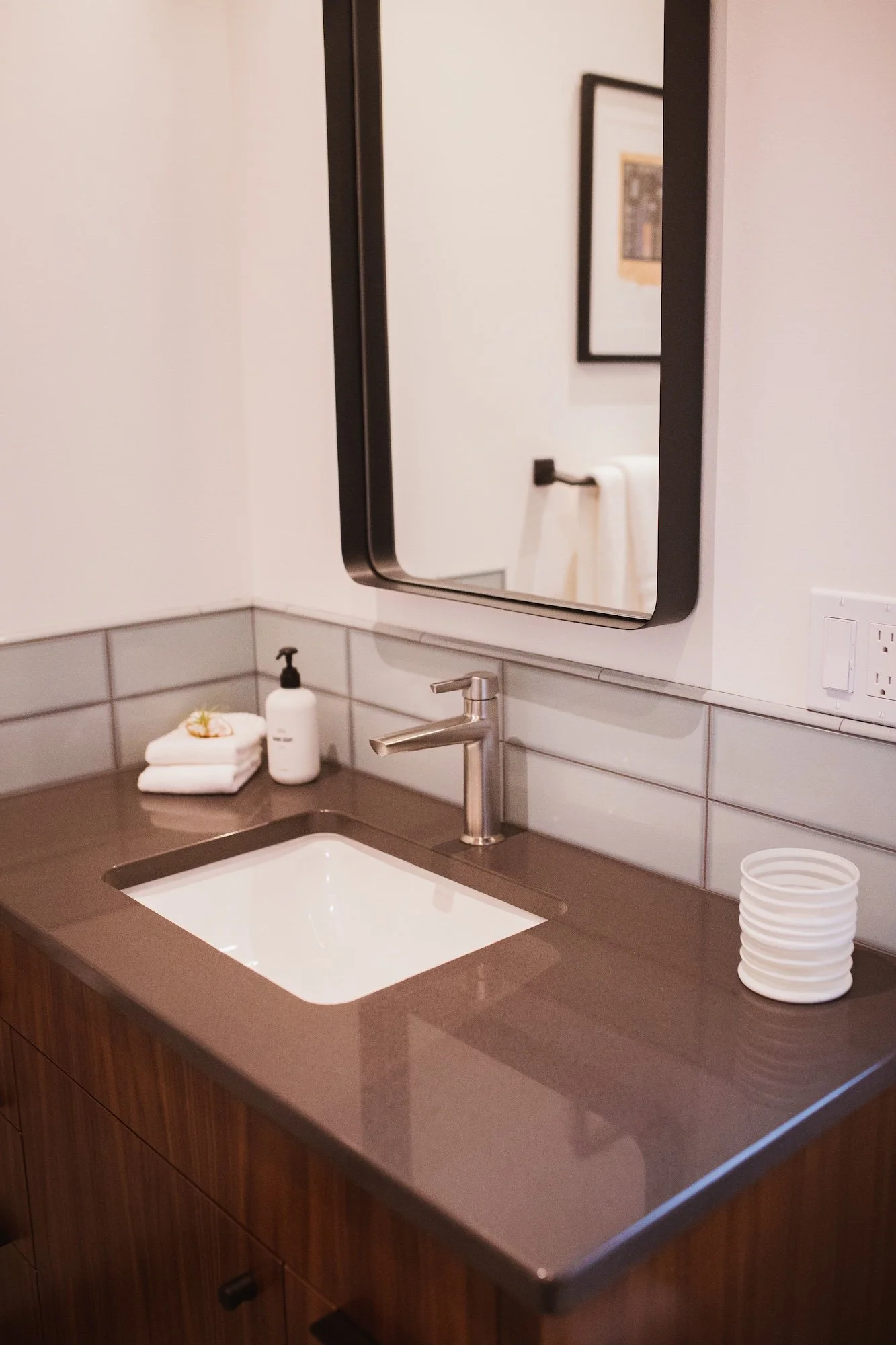 Bathroom sink with faucet, mirror, soap dispenser, white folded towels, and a stack of disposable cups.