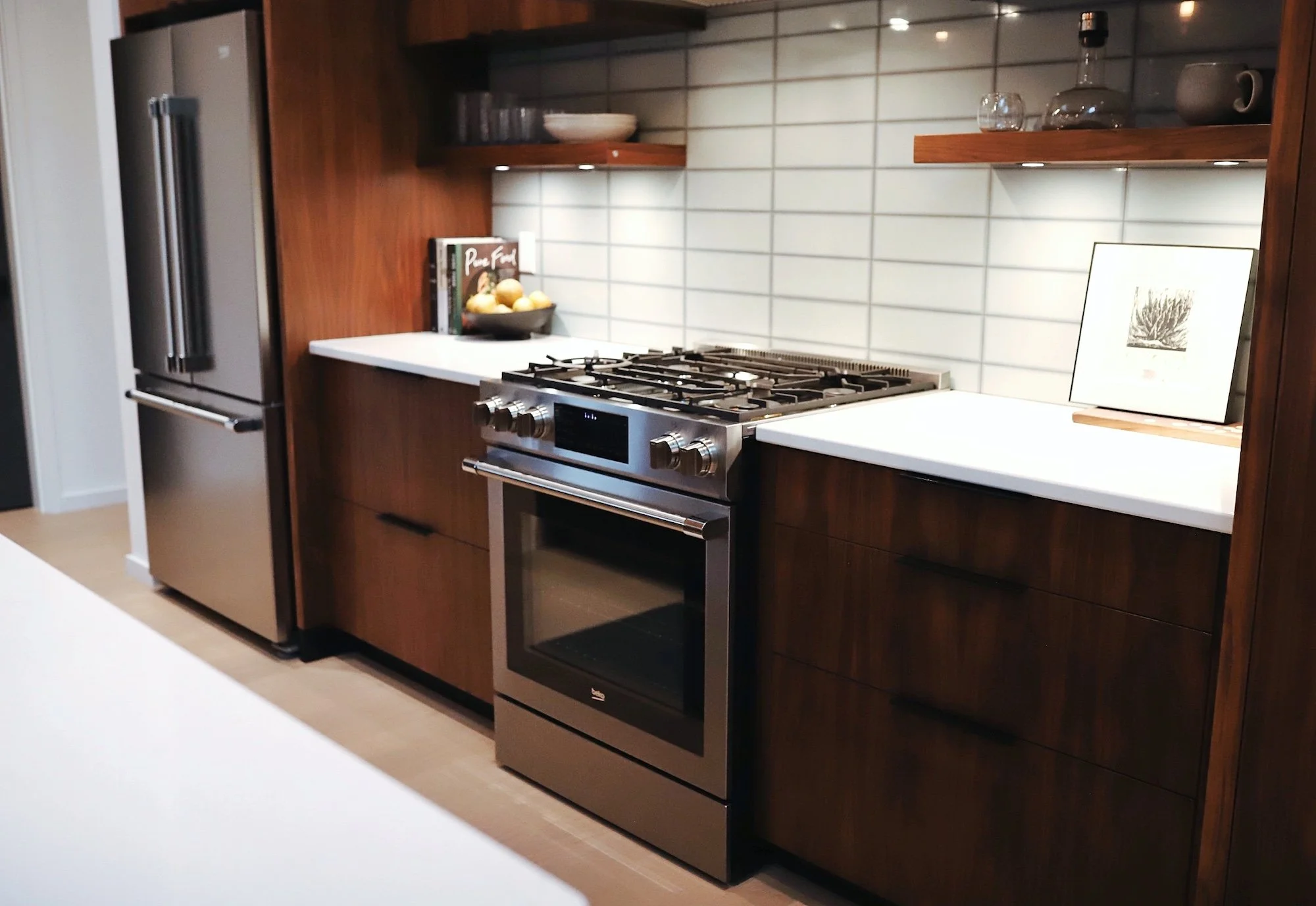 Modern kitchen with dark wood cabinets, a stainless steel refrigerator, a white countertop with a bowl of lemons, books, and decorative items, white subway tile backsplash, and a stainless steel oven and stove.