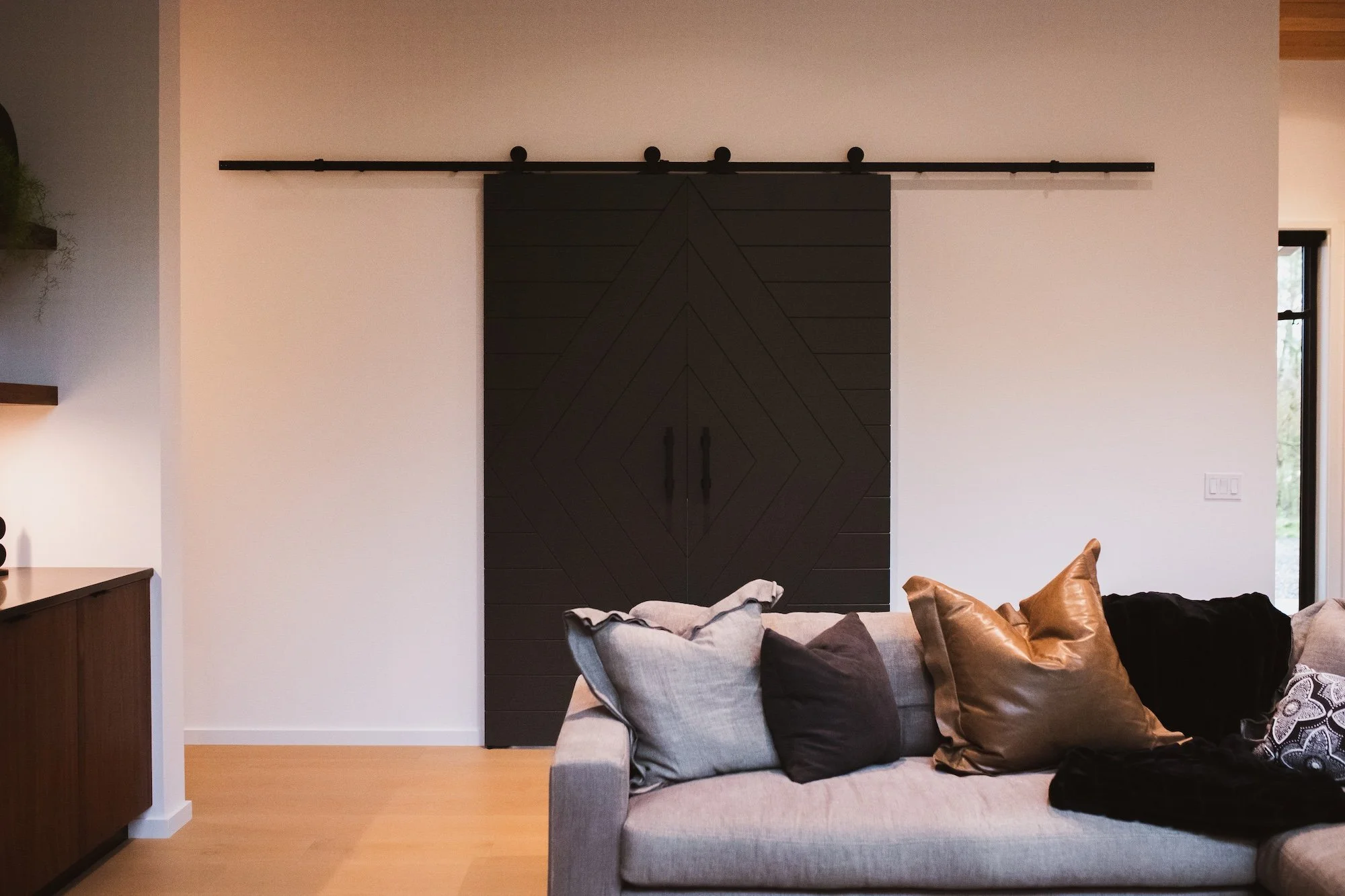 Living room with a gray sofa and decorative pillows, a black sliding barn door, and a window with natural light.