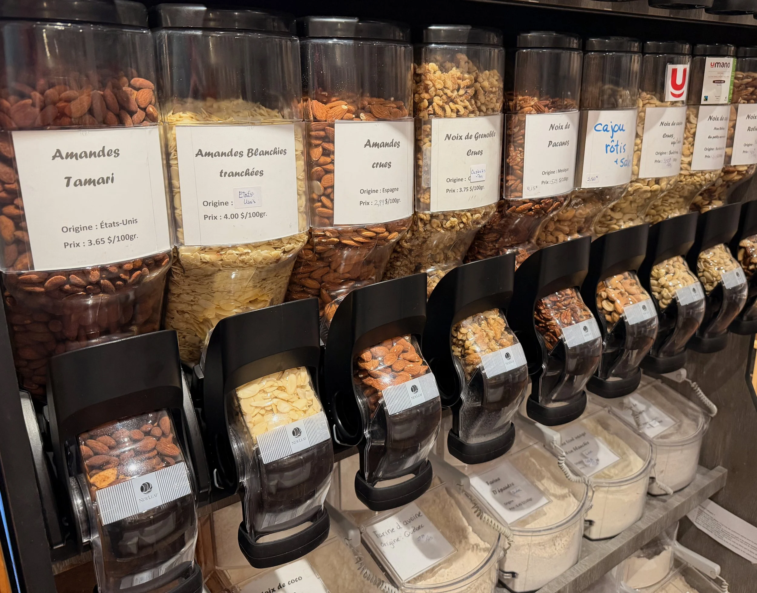 Rayonnage avec des contenants de différentes noix et amandes, étiquetés en français et anglais.