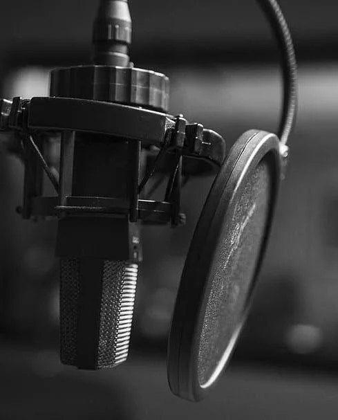 Black and white photo of a professional microphone with a pop filter in a recording studio.