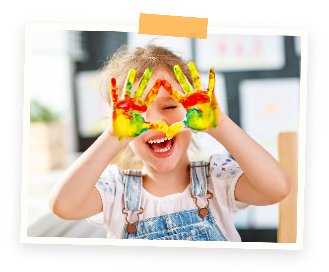 Paint time with messy hands. A young girl with painted hands making a frame around her eye and smiling indoors.