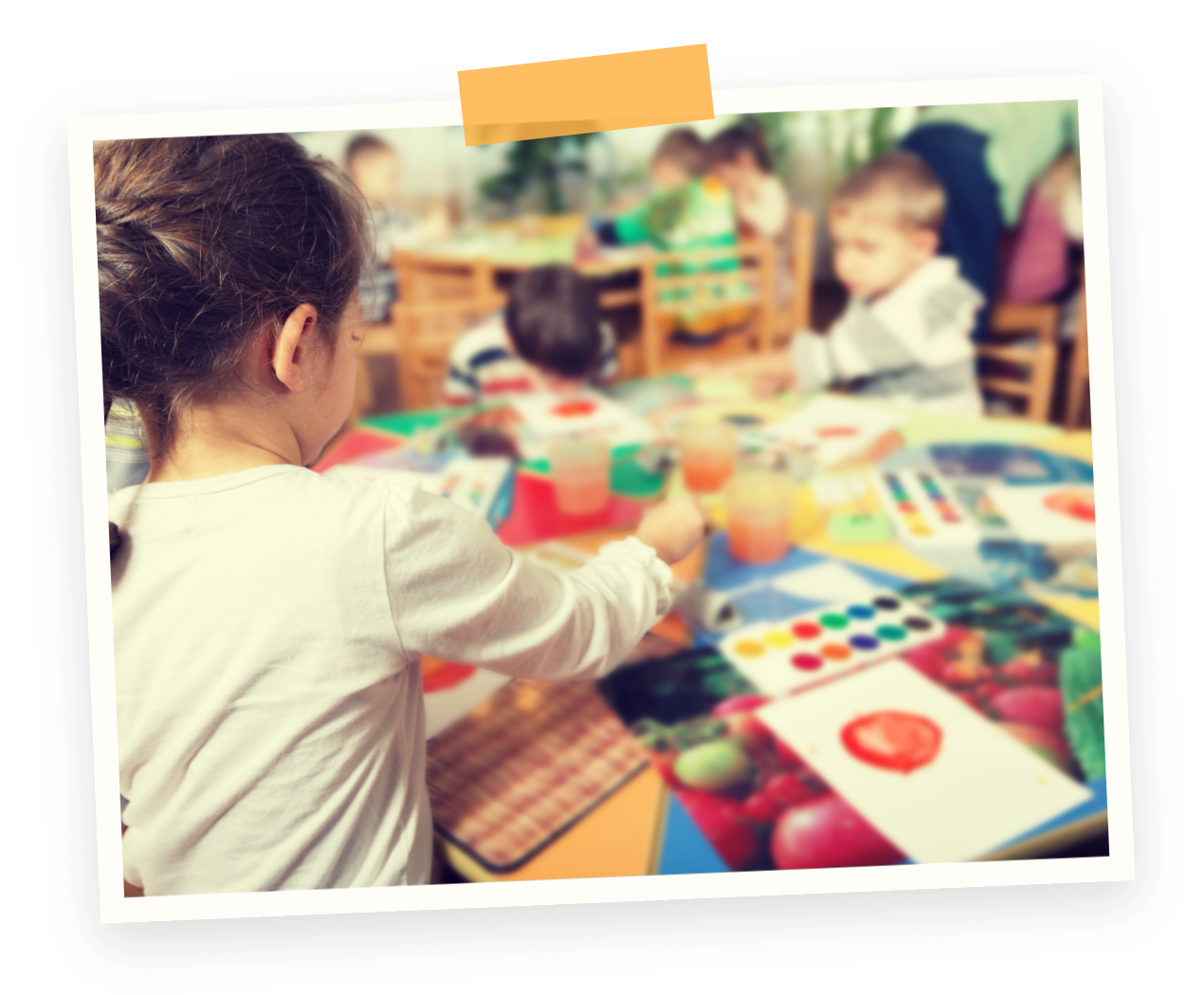 Children participating in a painting activity at a colorful table in a classroom or art room. Craft play time at our Marpole Preschool