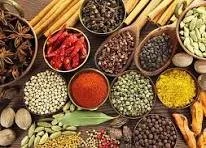 Wooden bowls filled with various spices and herbs, including red pepper flakes, black peppercorns, dried herbs, turmeric, and cumin, arranged on a wooden surface.