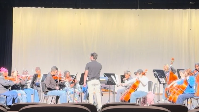 Youth orchestra practicing on stage with conductor in a theater.