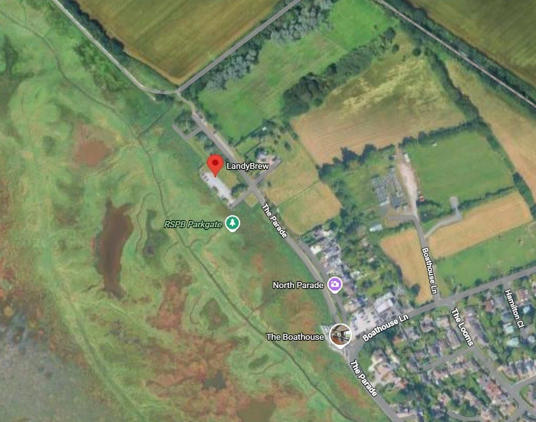 Satellite map showing an area with grassy fields, a pond, a park gate labeled RSPB Parkgate, and buildings including a location labeled LandyBrew near The Parade and Boathouse Lane.