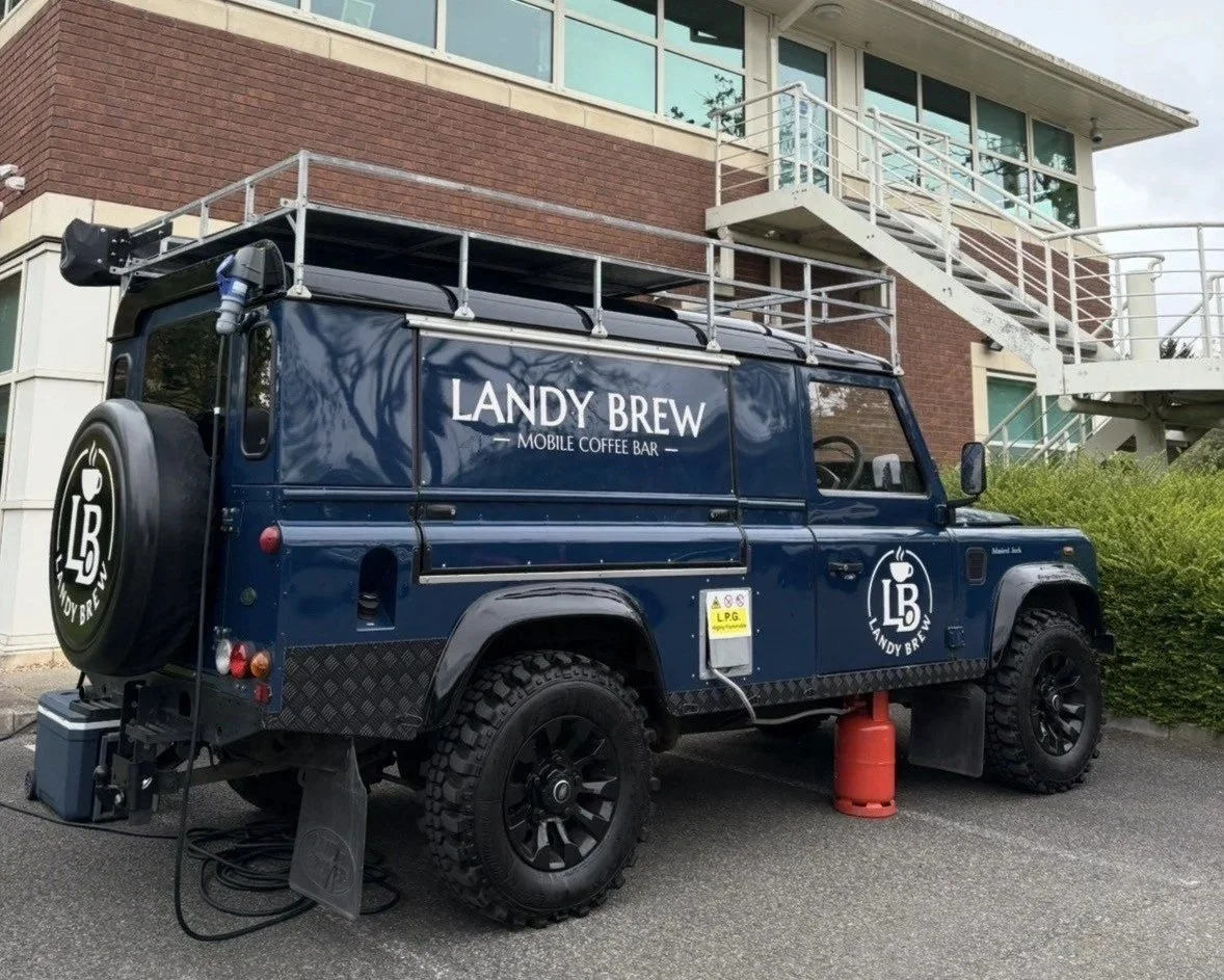 Blue Landy Brew mobile coffee bar vehicle parked outside a building with exterior staircase