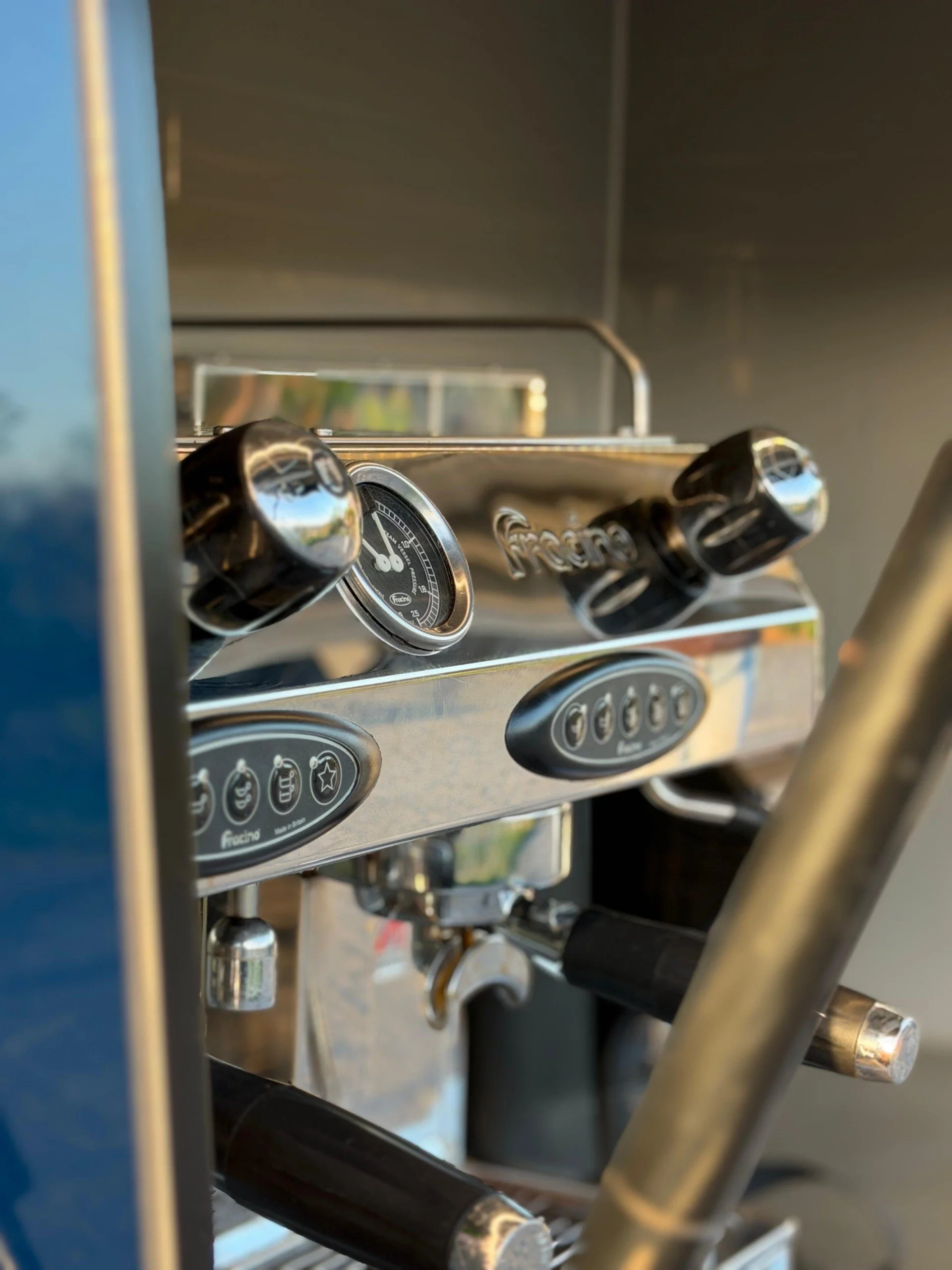 Close-up of a professional espresso machine's control panel and steam wand, with shiny metallic surfaces and black knobs.