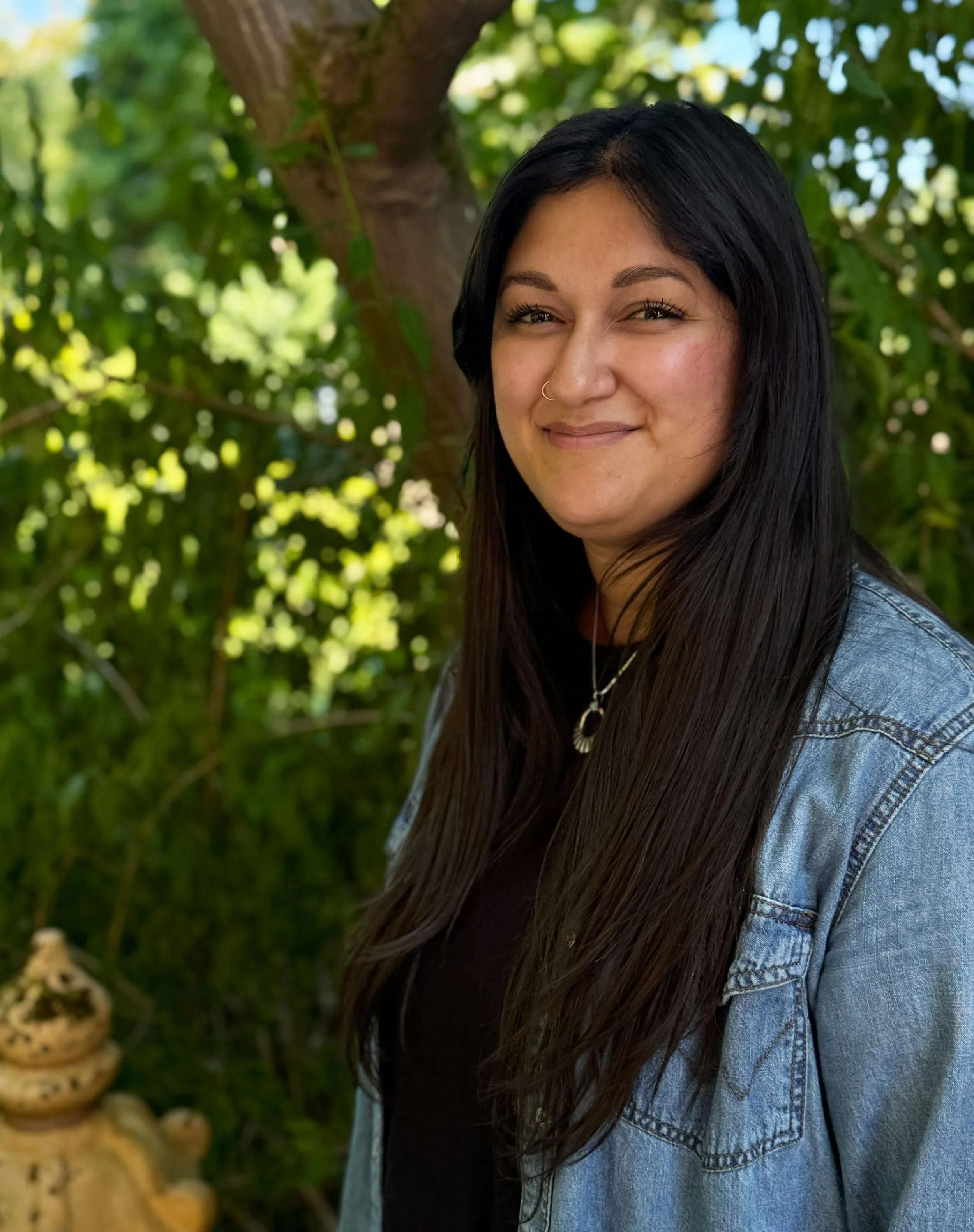 Deshika Bodhi-Jackson, owner of Bodhi Counseling and Wellness, standing outdoors in a green garden with trees and plants.
