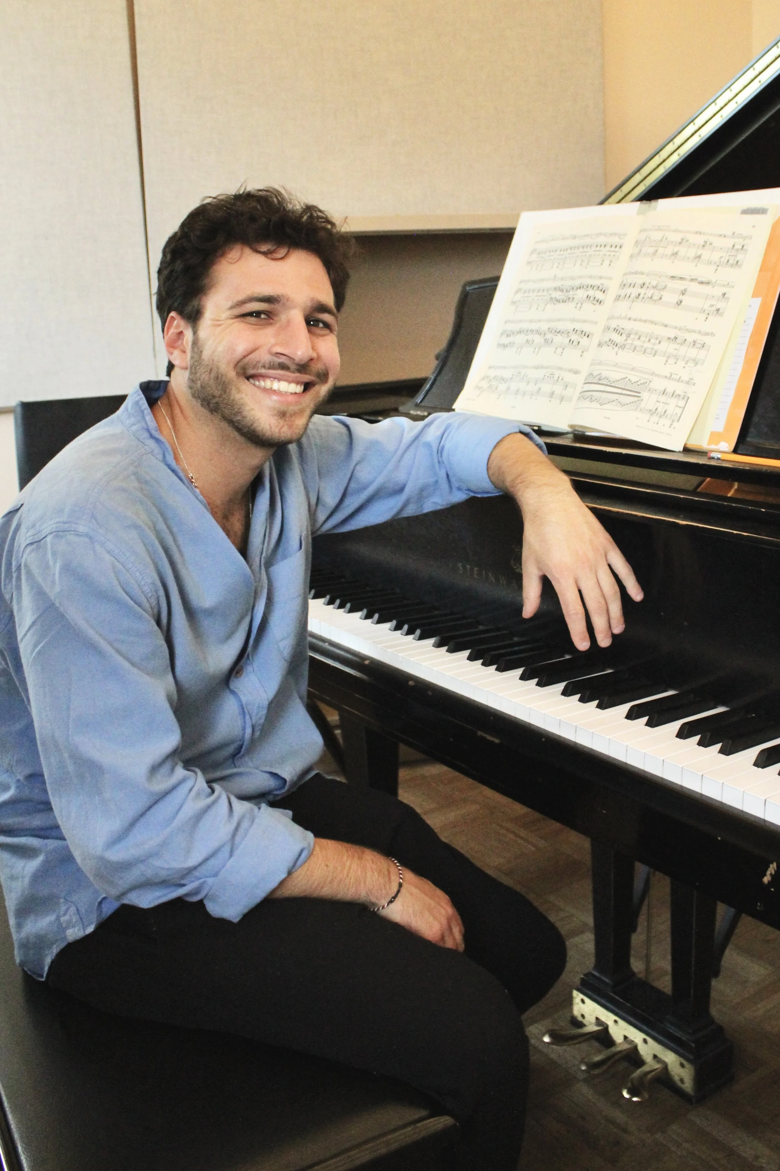 A man smiling and sitting at a piano with sheet music on the stand.