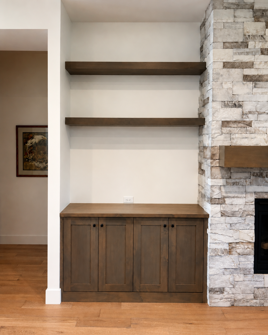 Custom built-in cabinet and floating shelves installed beside a stone fireplace by Crown Point Finish near Boise, Idaho.