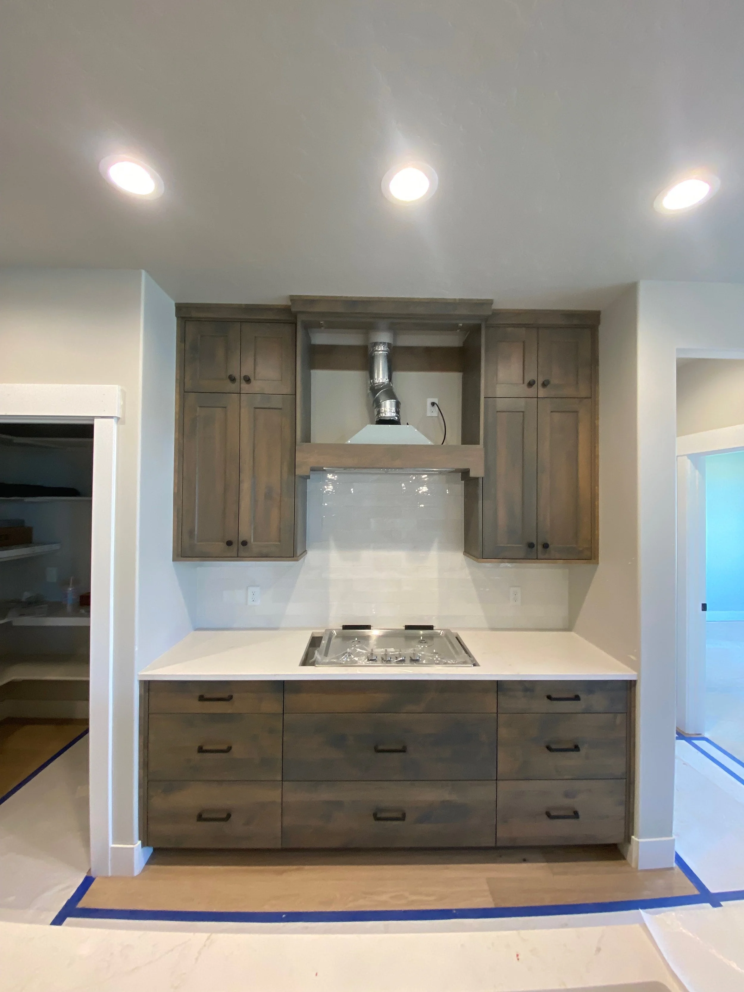 Kitchen with light wood cabinets, white countertop, and a built-in stove. There are recessed ceiling lights and a duct vent above the stove. The surrounding walls are painted in light neutral colors.
