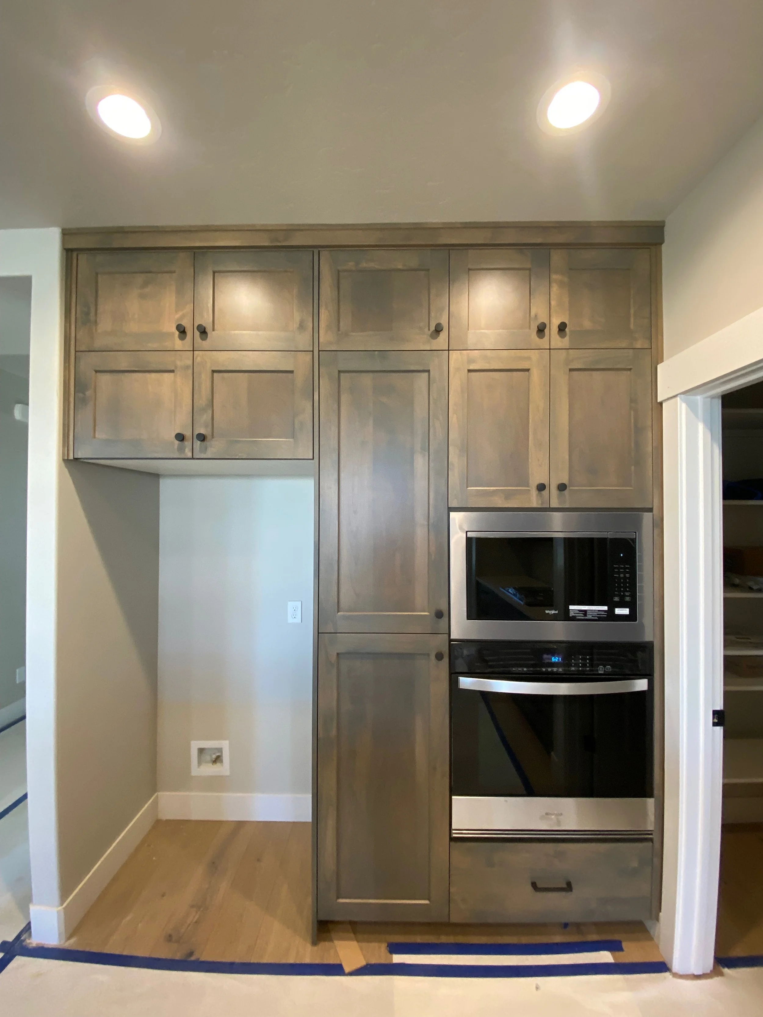 Kitchen with wooden cabinets and built-in stainless steel microwave and oven. Hardwood floor and a small section of blue tape on the floor.