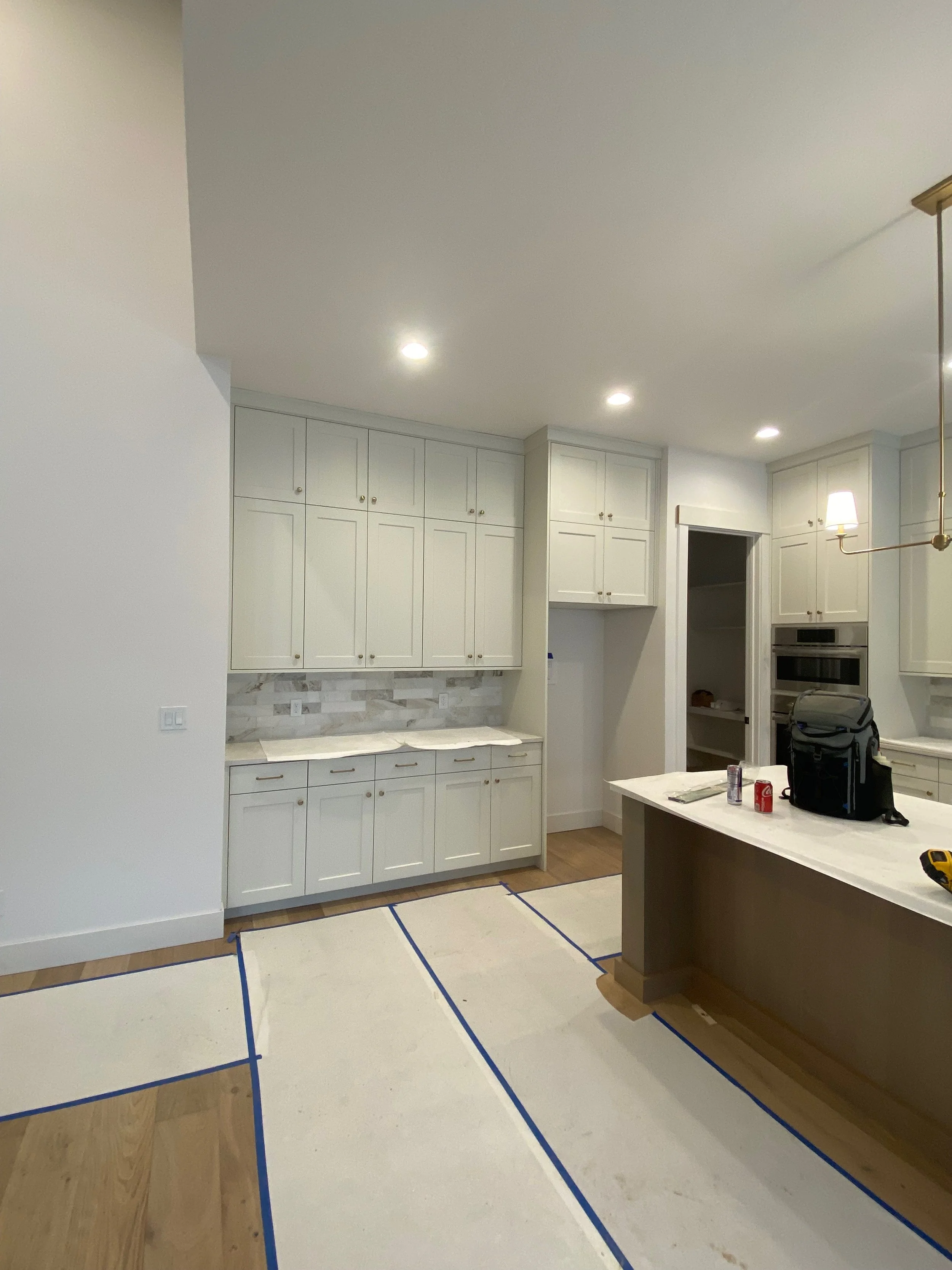 Kitchen with white cabinets, marble countertops, recessed lighting, a partially finished floor with blue painter's tape, and an island with personal items on it.