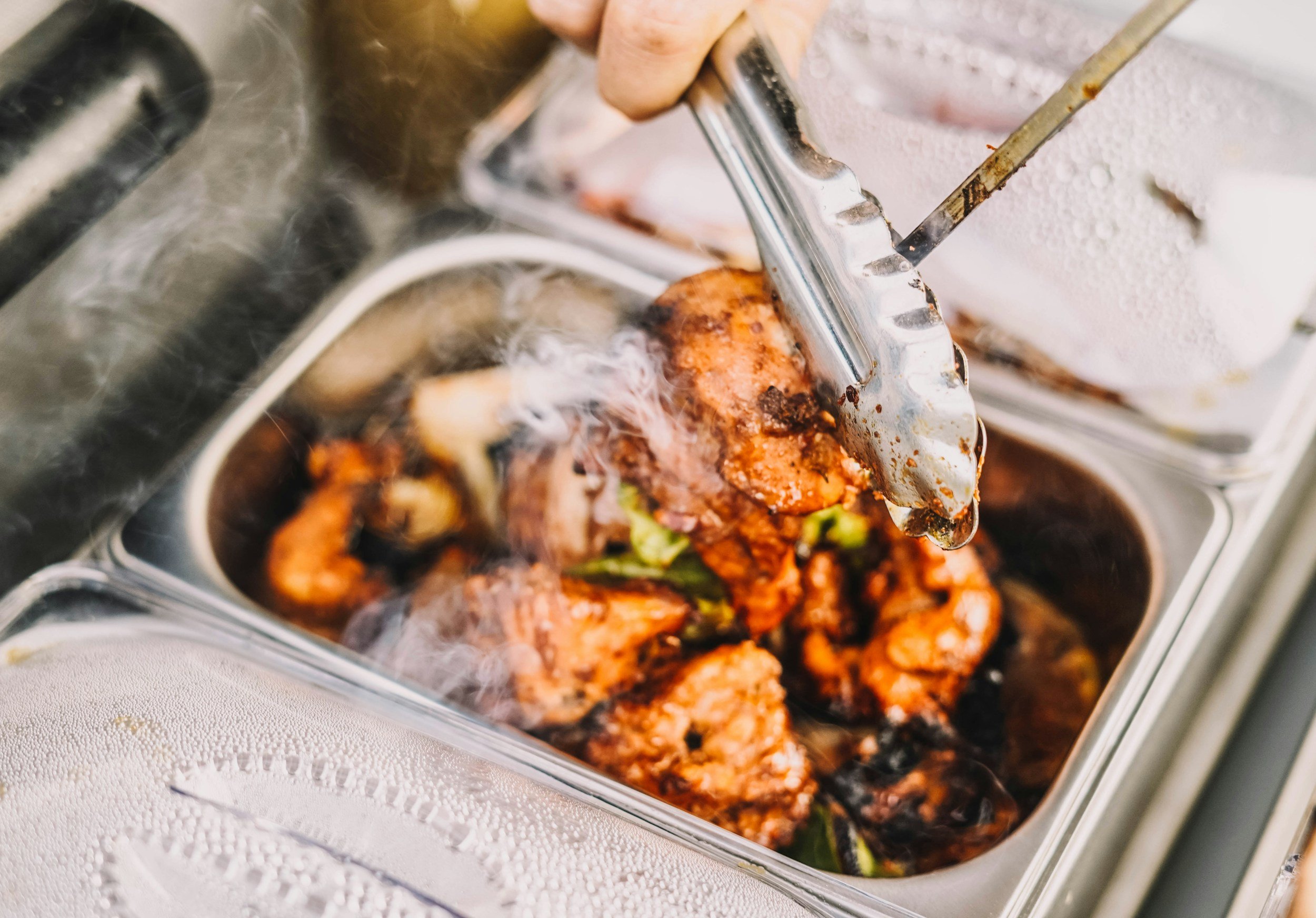 Food being served with tongs from a metal pan, possibly at a buffet or catering event.