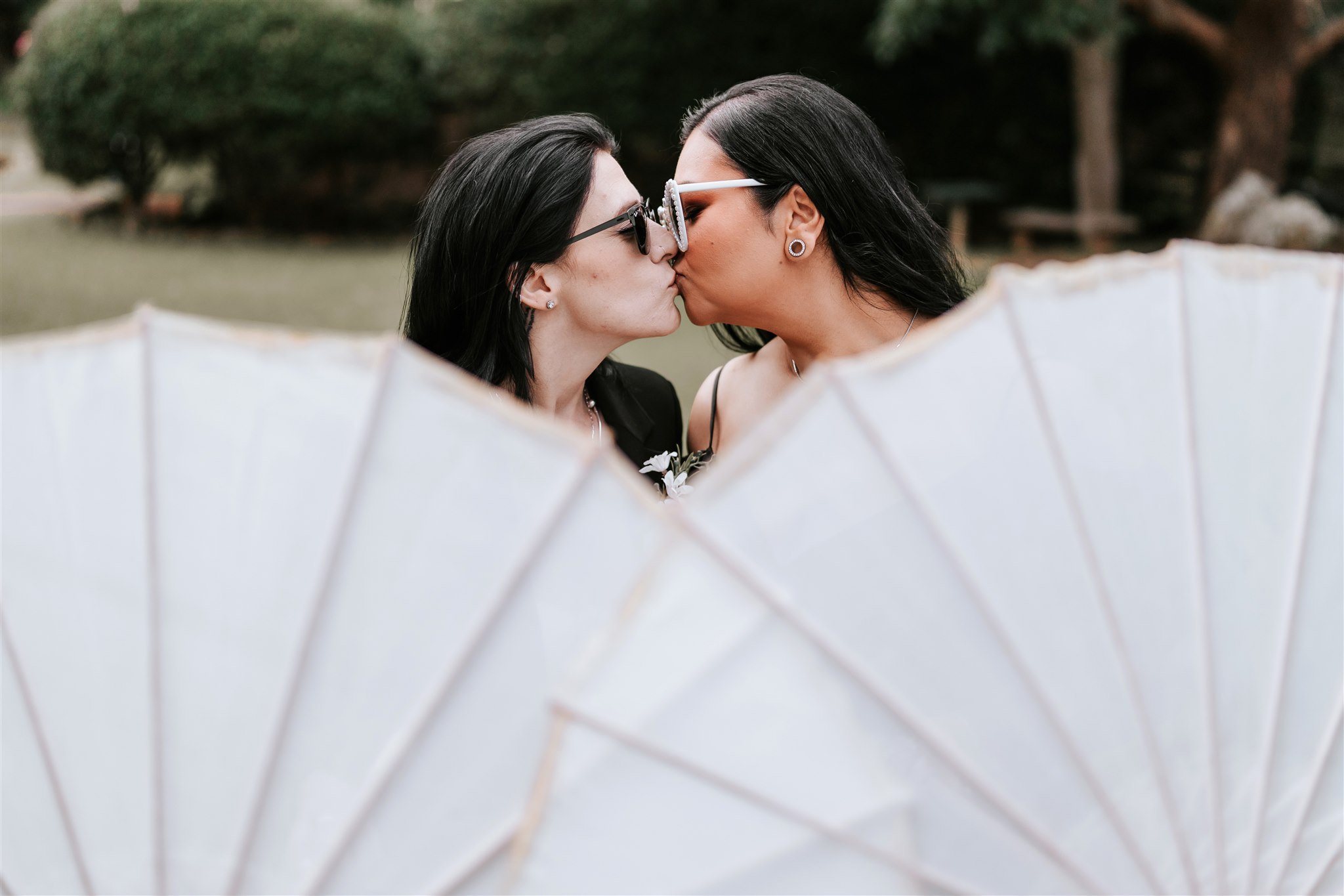 Two women sharing a kiss outdoors, seen through a white paper lantern.