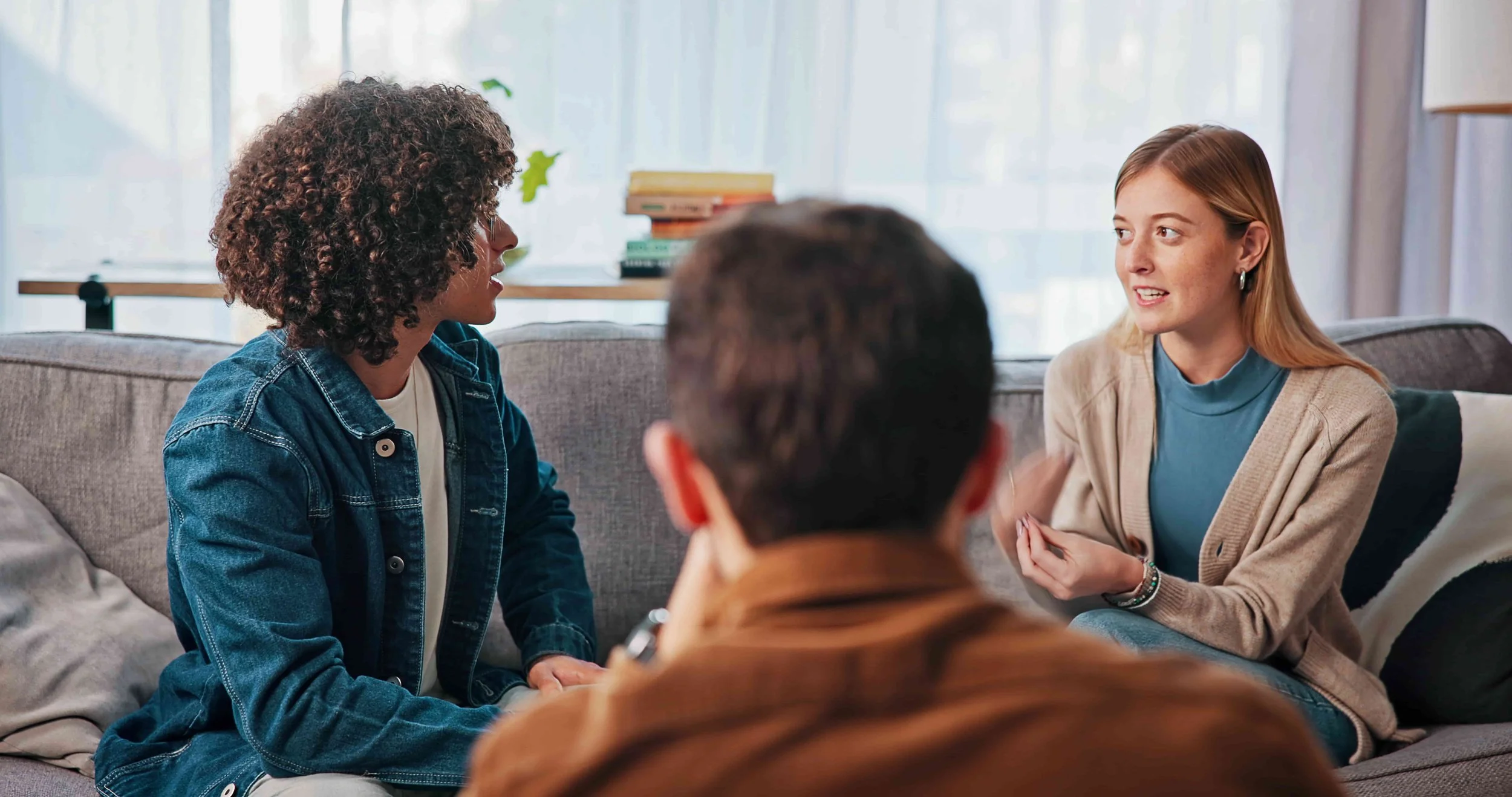 People having a conversation in a living room have a discussion with one woman talking while others listen.