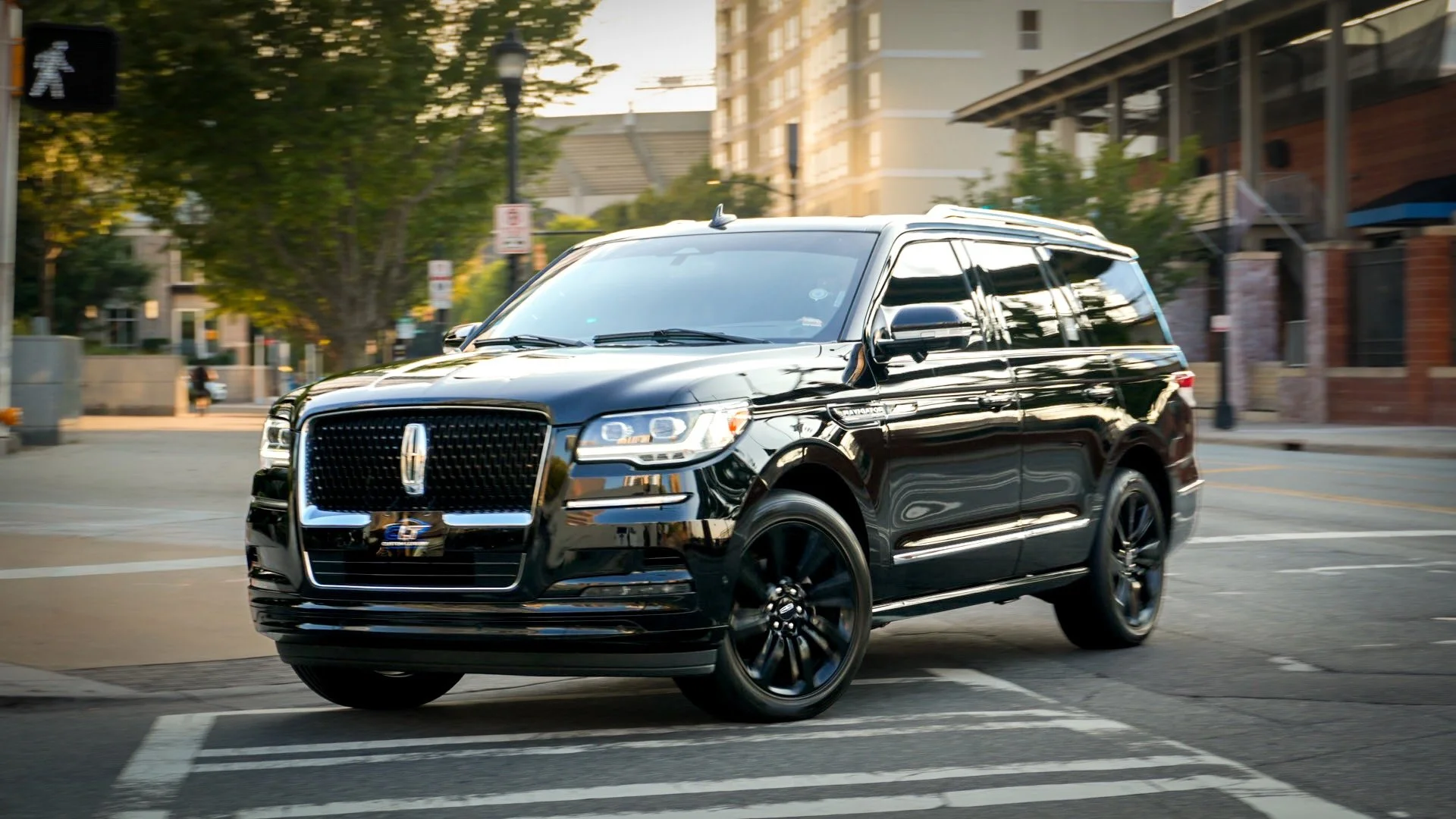 A black luxury SUV driving through an urban street at sunset, with buildings and trees in the background.