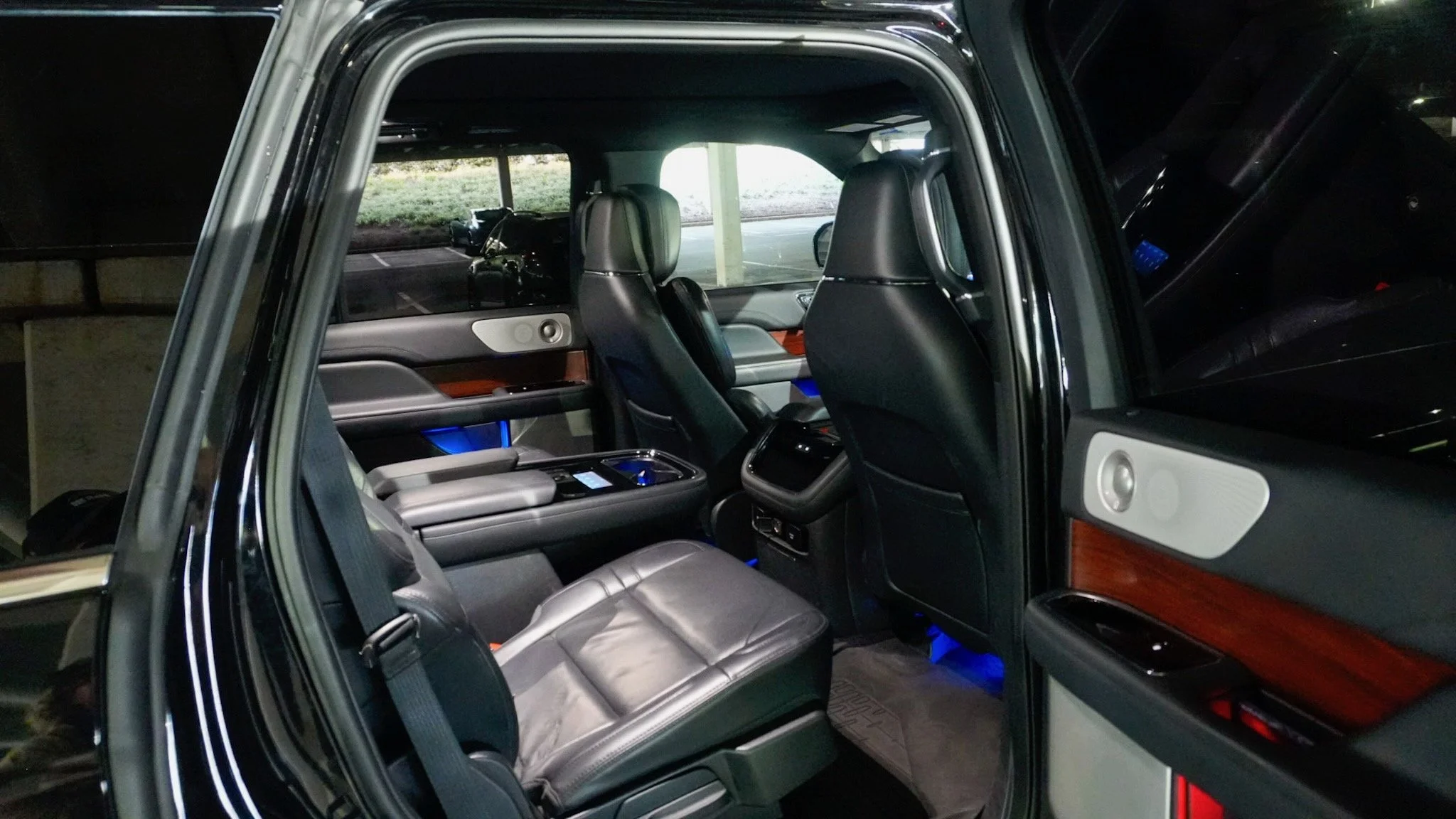 The interior of a black luxury SUV at night shows leather seats with illuminated ambient lighting, wood panel accents, and a panoramic sunroof.