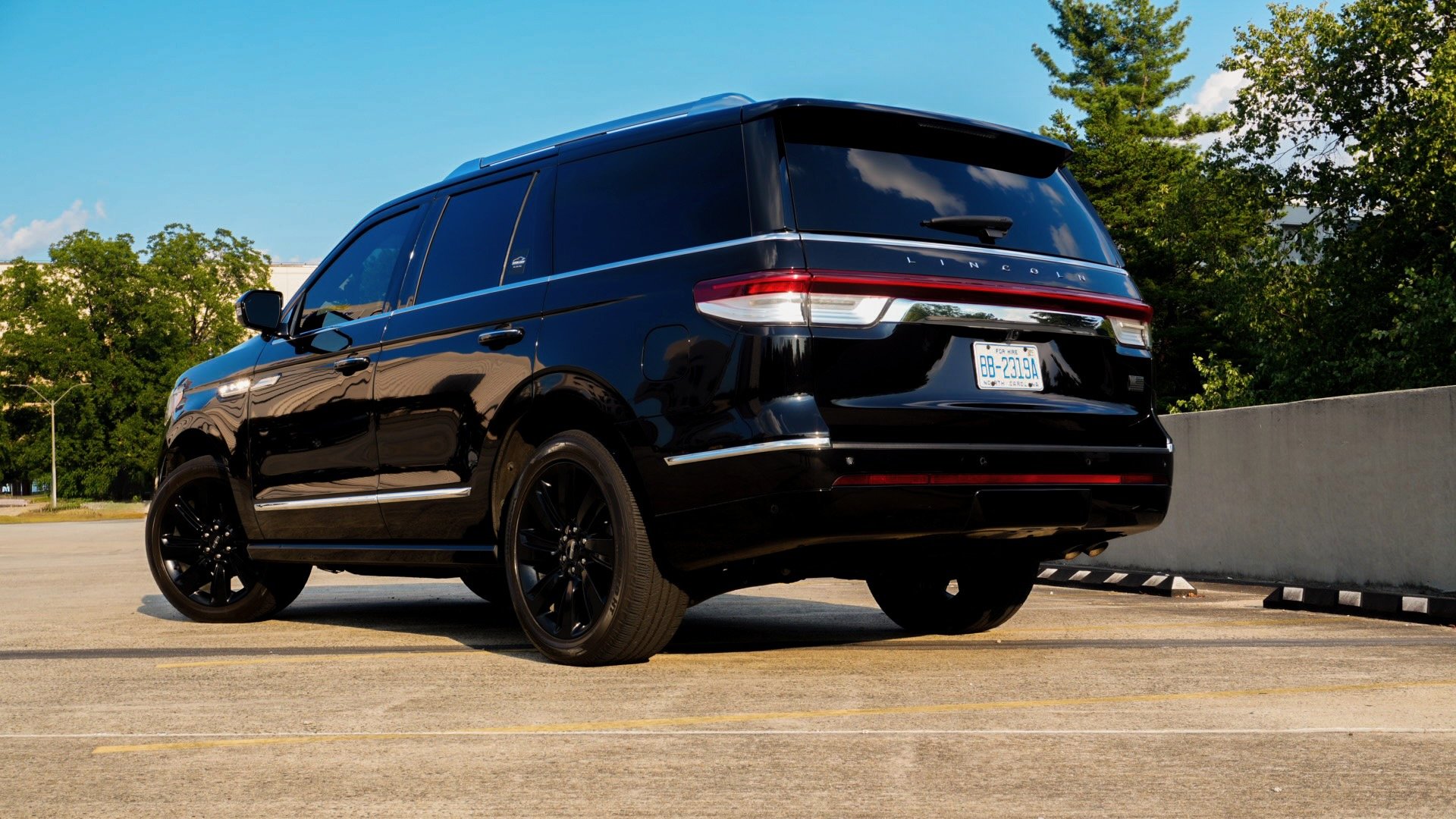 Black Lincoln SUV parked in an empty parking lot with trees and a blue sky in the background.