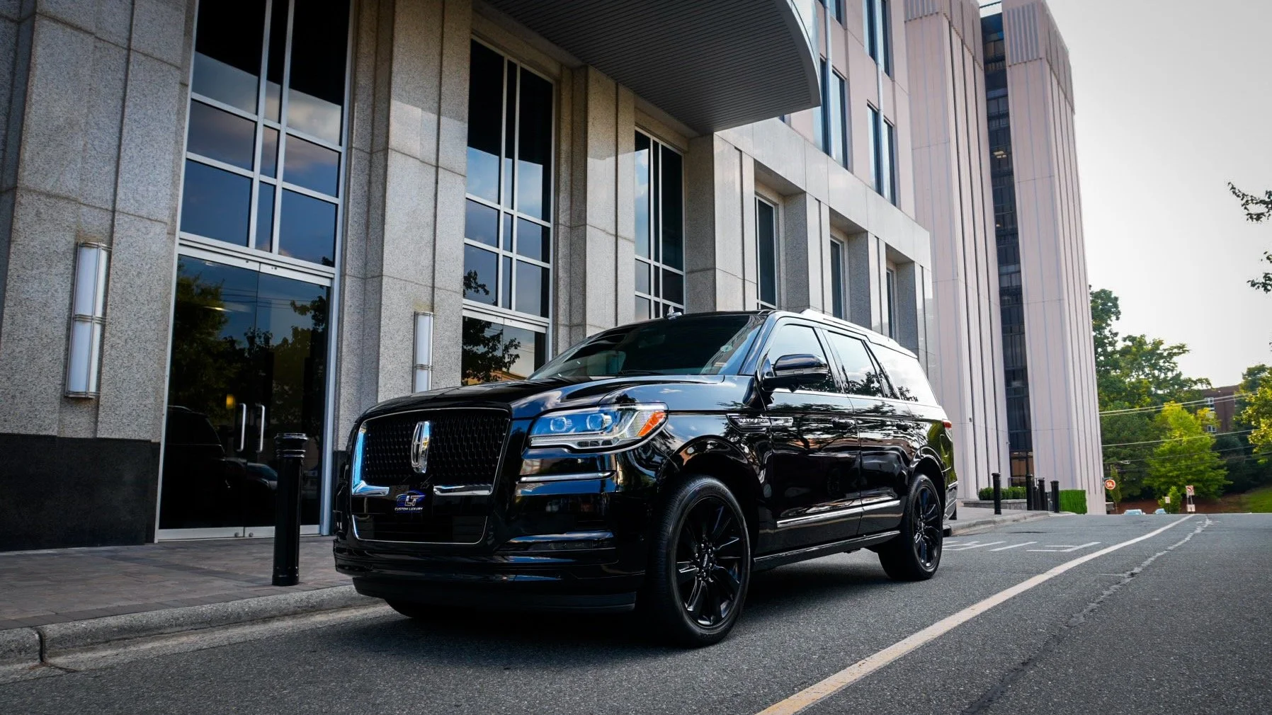 Black luxury SUV parked on city street in front of modern office building with large glass windows and concrete facade.