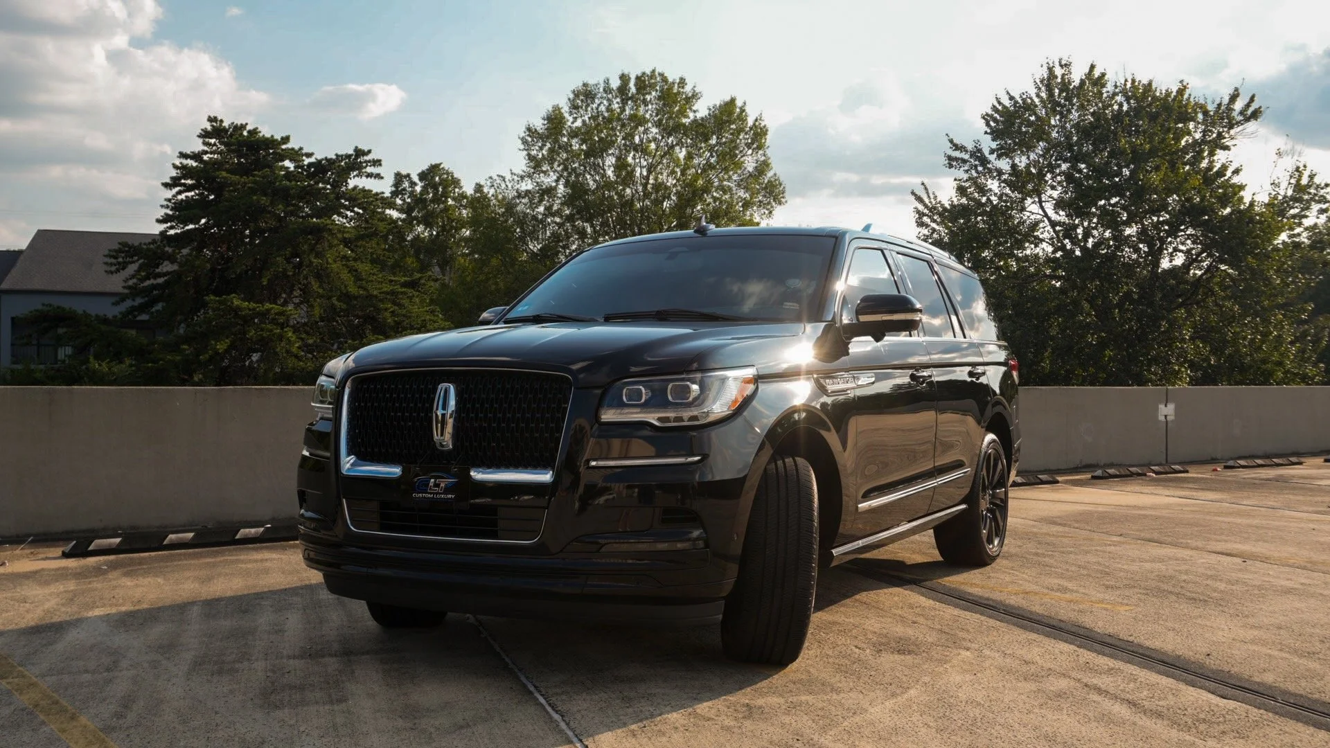 Black Lincoln Navigator SUV parked on a rooftop parking lot during daylight with trees and a partly cloudy sky in background.