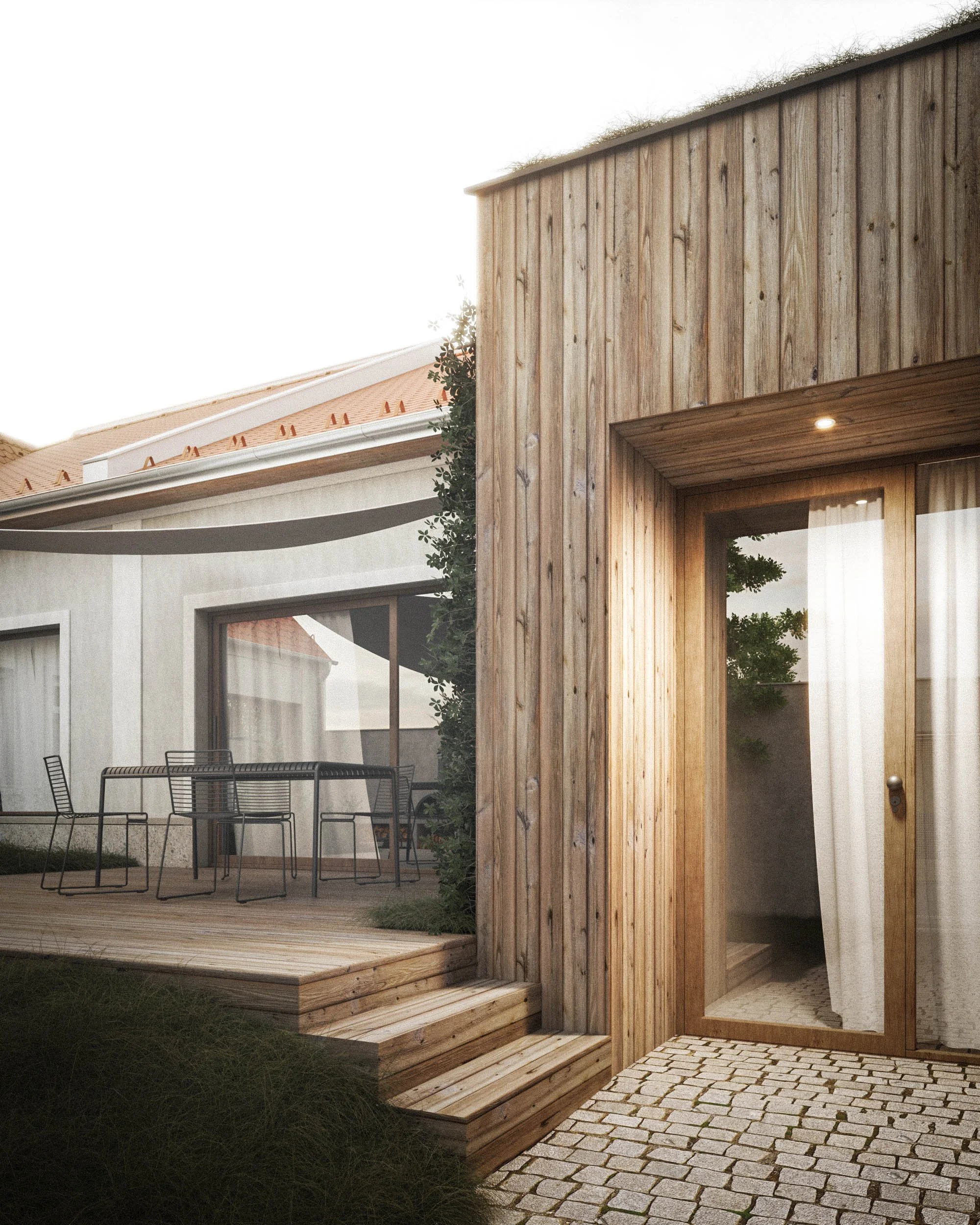 Exterior of a modern house with a wooden facade, large glass windows, and a patio area with chairs. There is a small wooden deck and a brick pathway leading to an entrance. The house has a light-colored wall, and there are trees reflected in the glass. Overhead lighting is visible near the entrance.