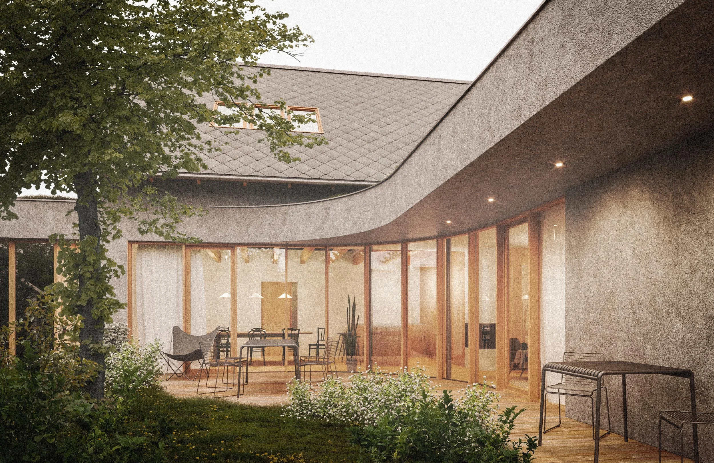 Modern house with large, curved glass windows and a gray textured exterior wall, surrounded by greenery and outdoor seating, lit with warm interior lighting.