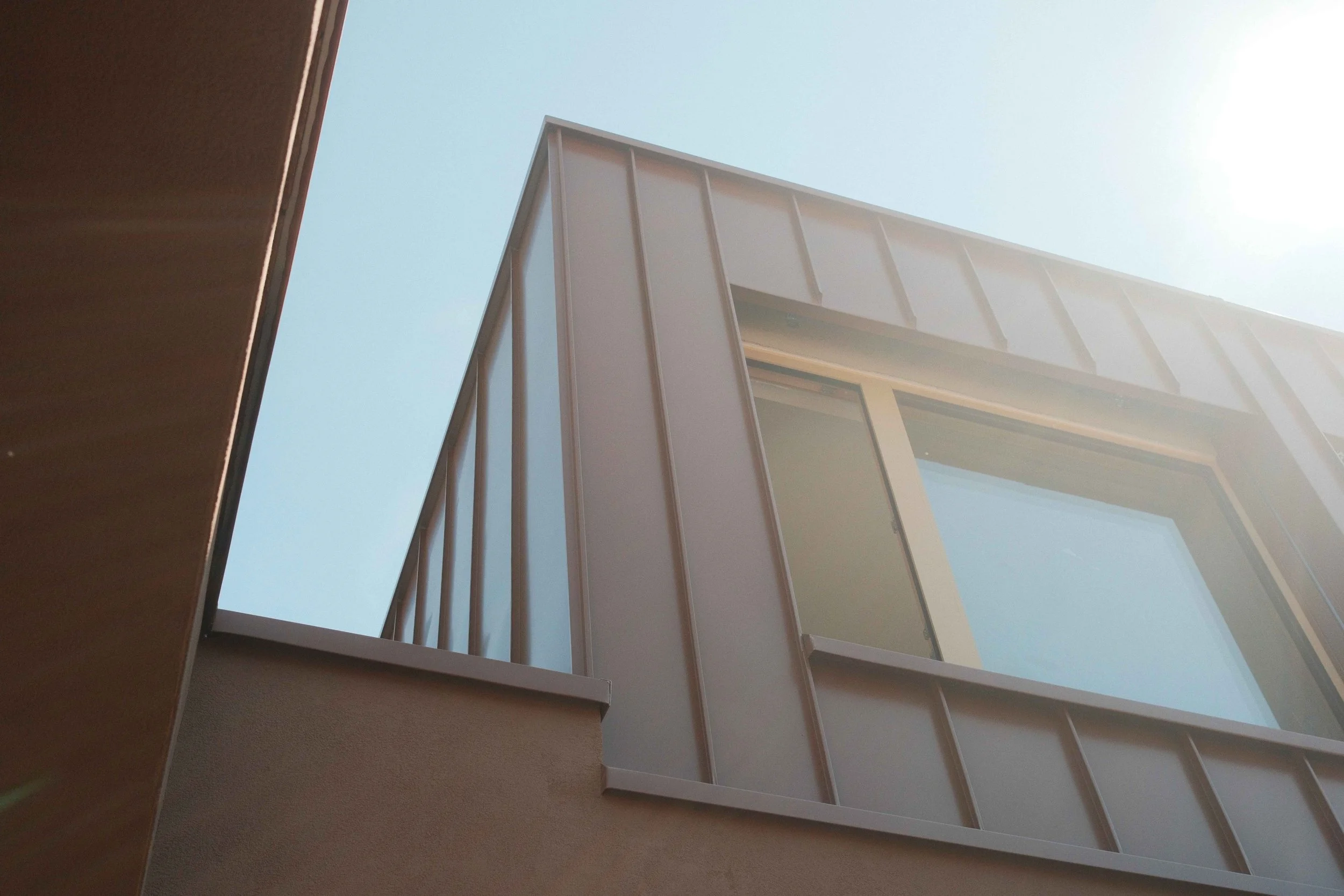 Looking up at modern building with glass windows and metal panels, seen from an angle with clear sky background.