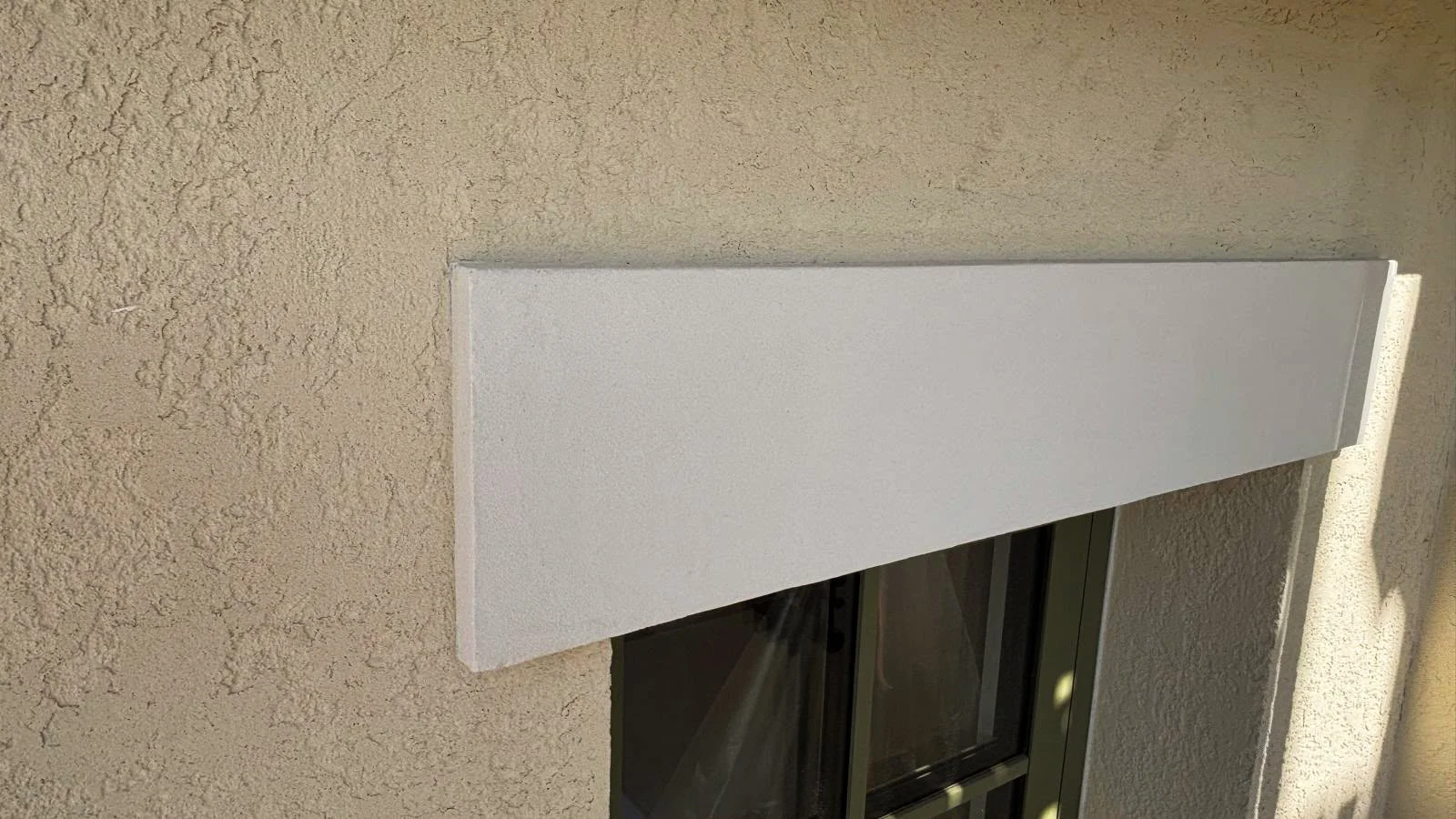 Close-up of a window with beige textured wall and white exterior sconce or trim above it.